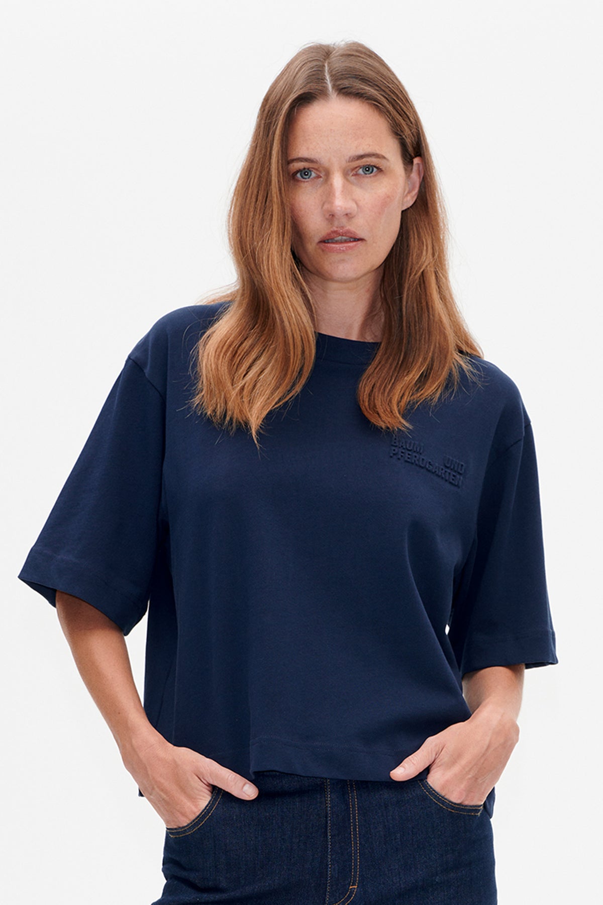 Front view of a model wearing a navy short-sleeved T-shirt with subtle raised lettering on the chest.