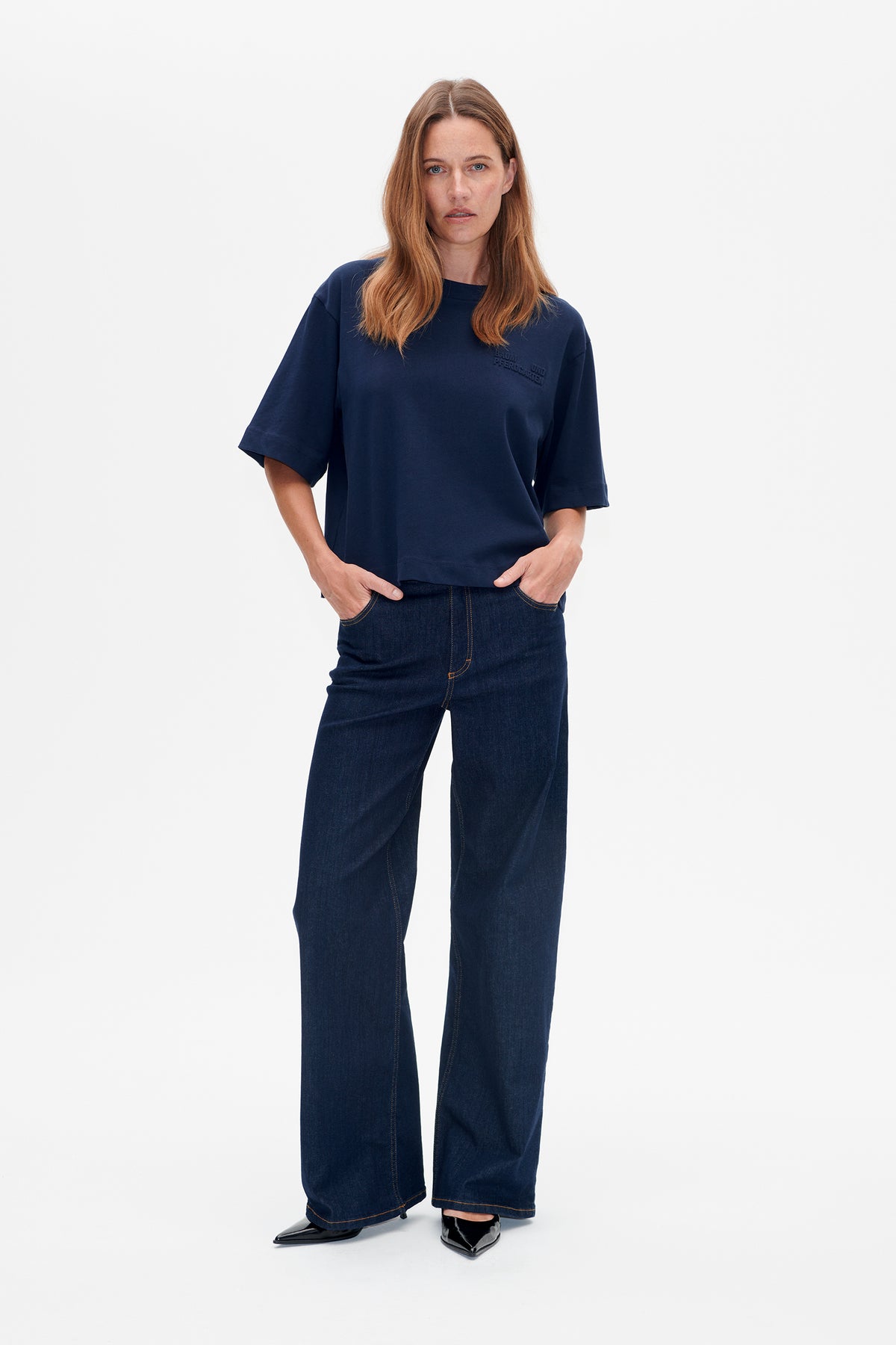 Model wearing a navy oversized short-sleeve T-shirt with a subtle chest logo and dark wide-leg jeans, shown from the front.