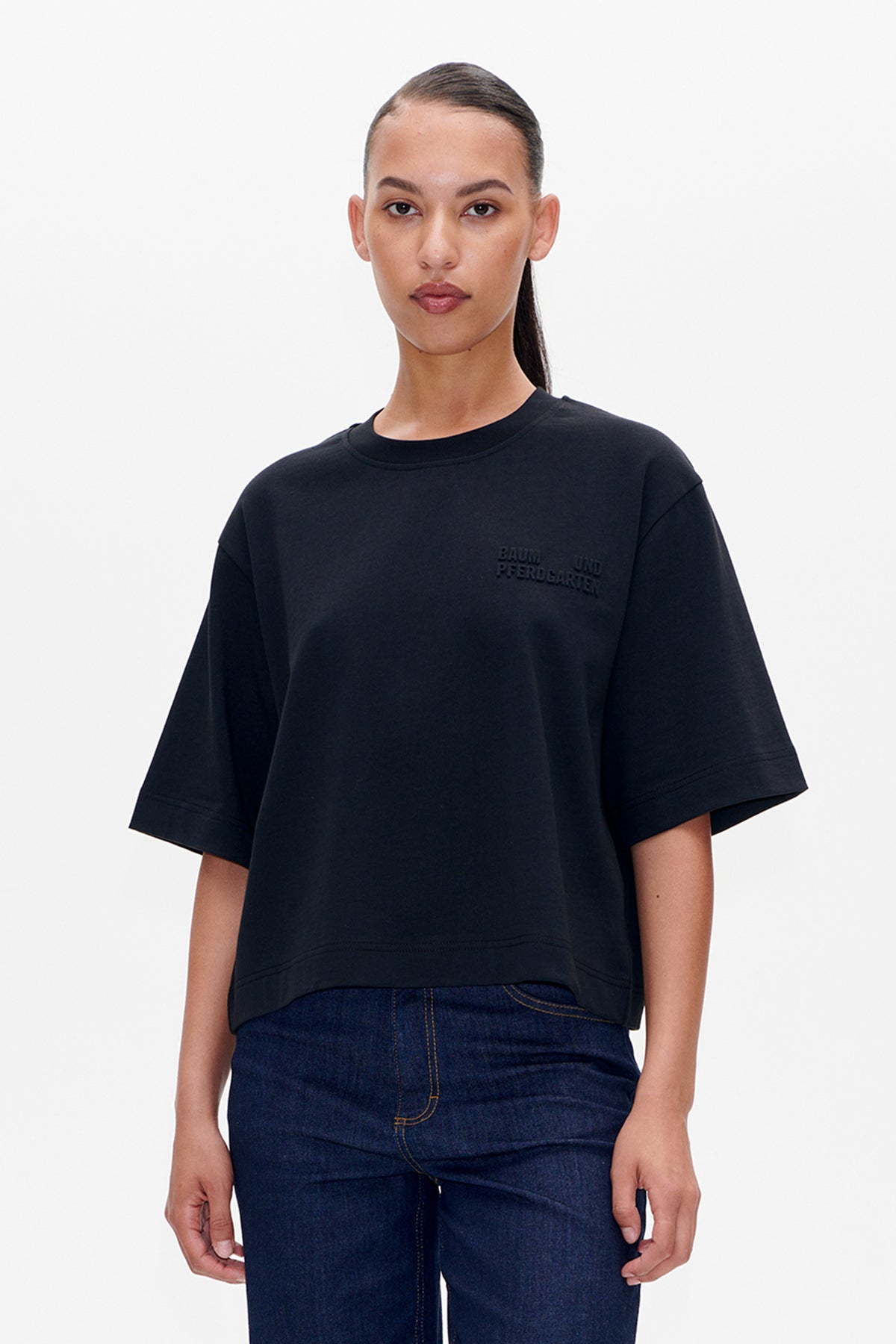 Front view of a black short-sleeved crew-neck T-shirt with subtle tonal chest lettering, paired with dark blue jeans.