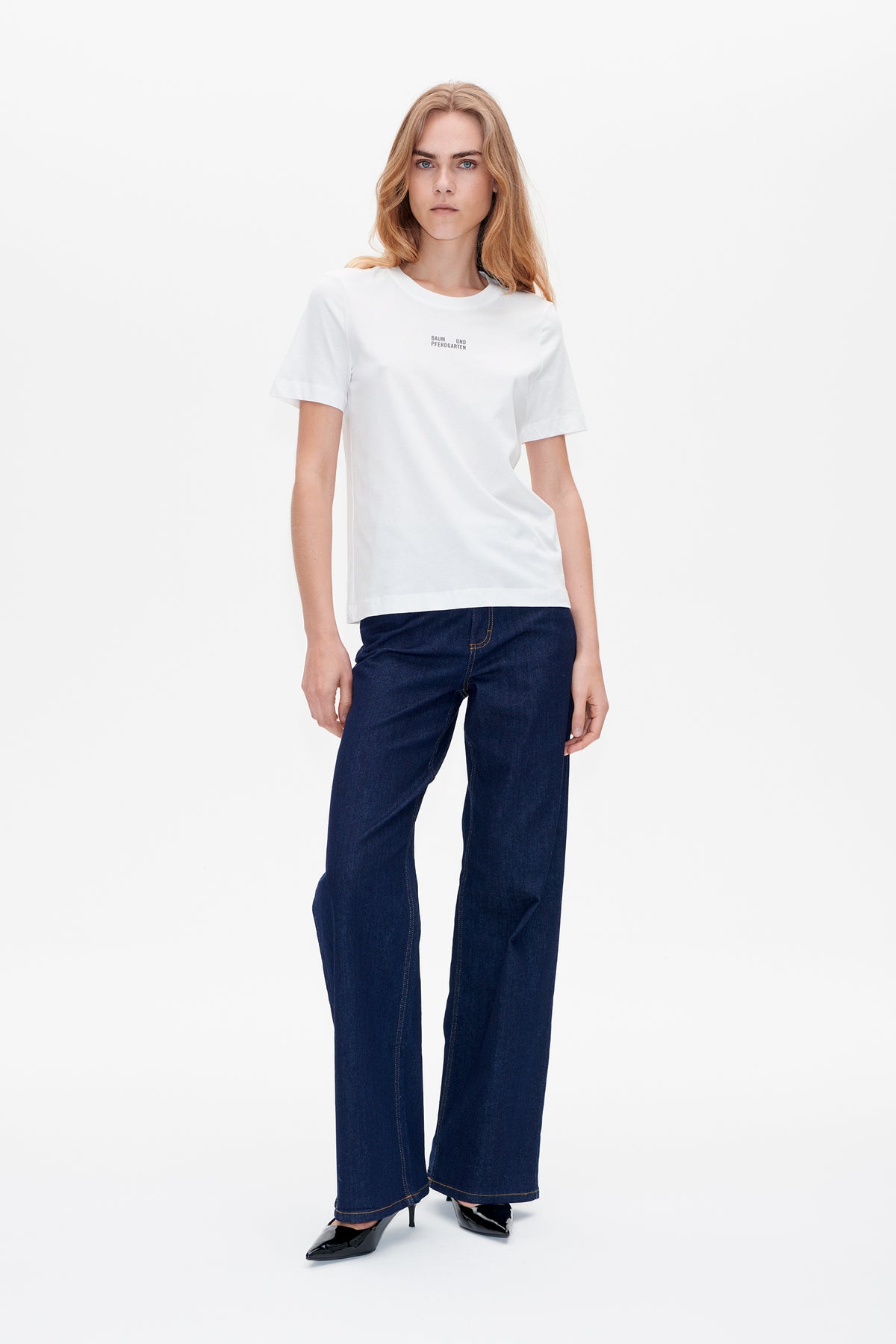 Front view of a white short-sleeved T-shirt with small chest lettering, styled with dark blue wide-leg jeans.