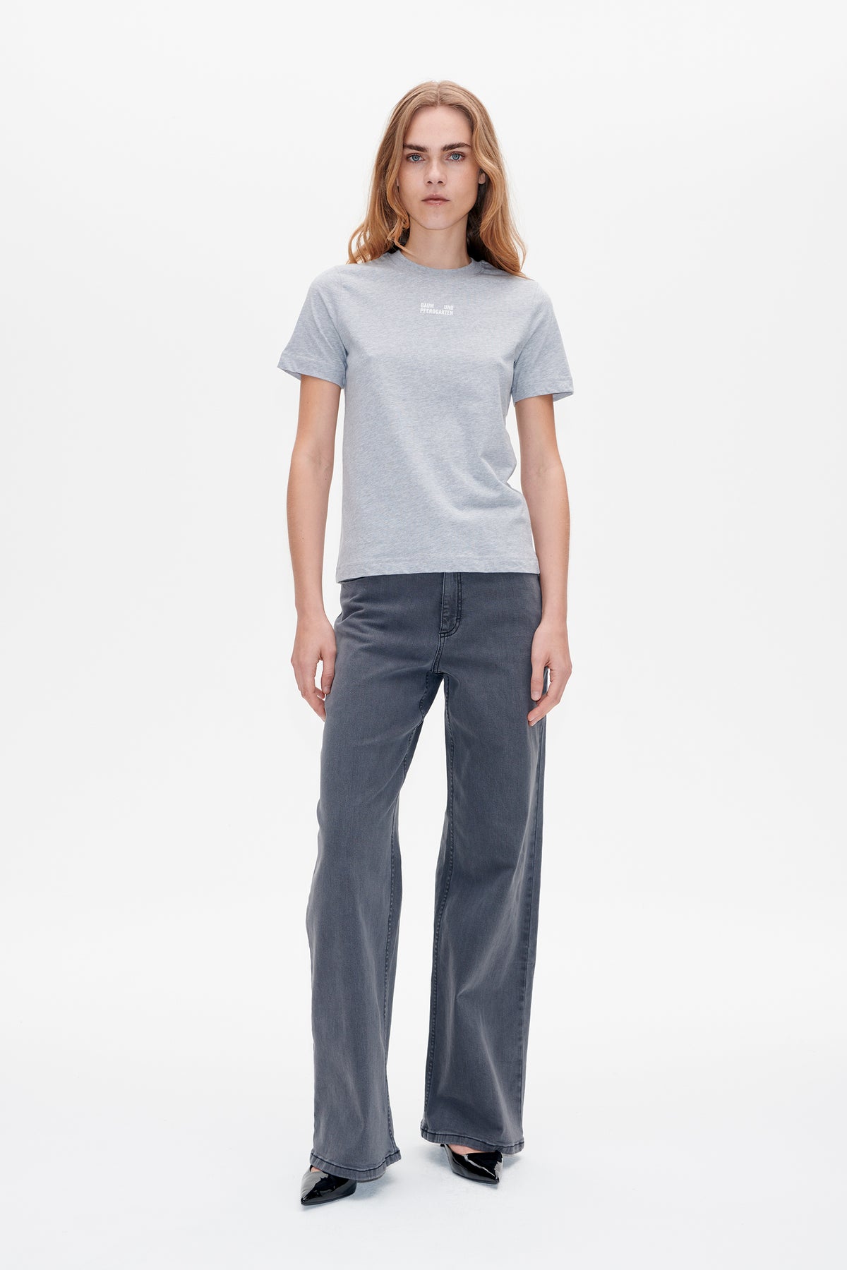 Model wearing a light grey short-sleeved T-shirt with a small white chest logo and dark grey wide-leg jeans, front view.