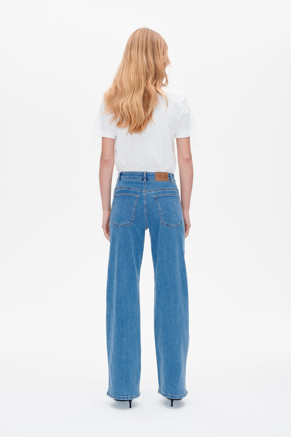 Back view of a model wearing a plain white short-sleeved T-shirt and blue wide-leg jeans with two back pockets.