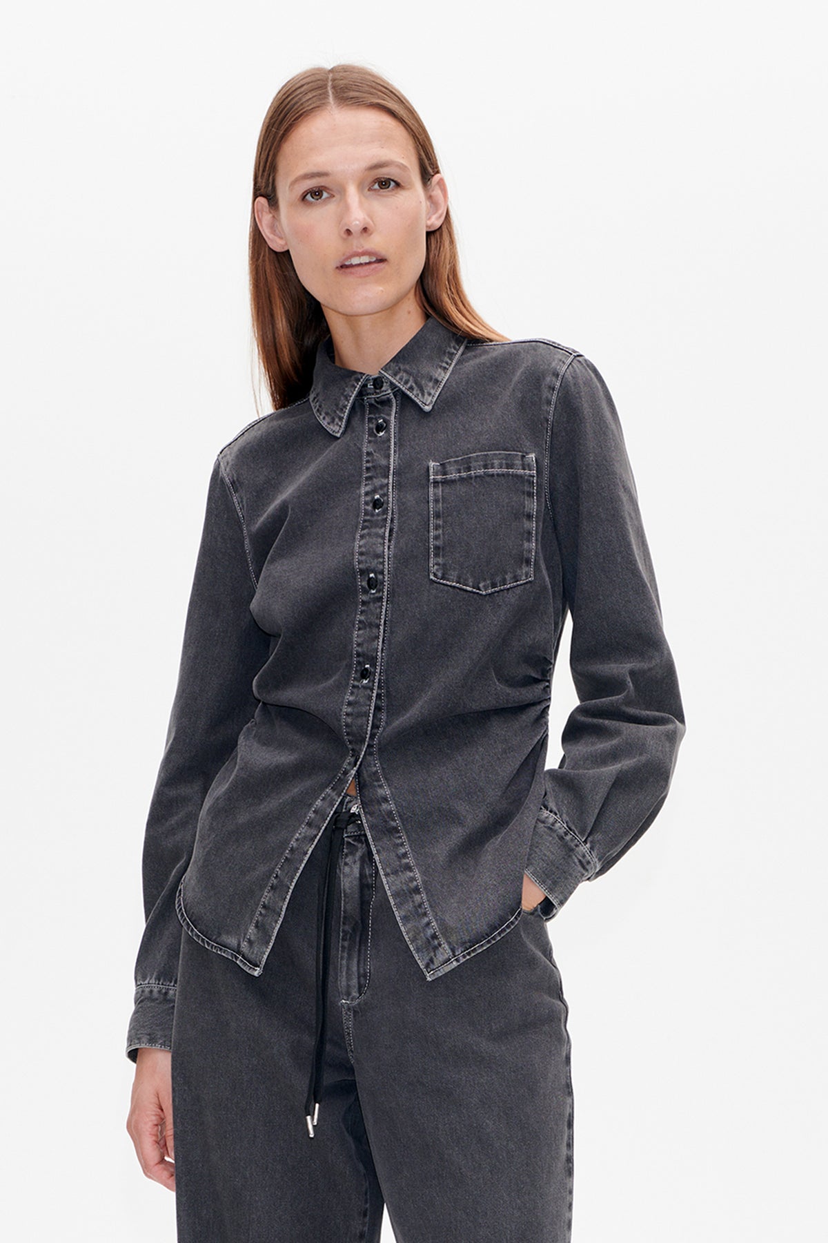 Vooraanzicht van een donkergrijs gewassen denimblouse met puntkraag, knoopsluiting, borstzak en lange strikbanden aan de voorkant.