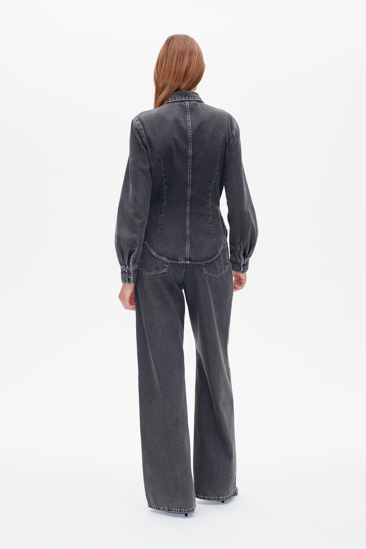 Achteraanzicht van een model dat een antracietgrijze denimblouse met afgeronde zoom en wijd uitlopende, bijpassende jeans draagt.