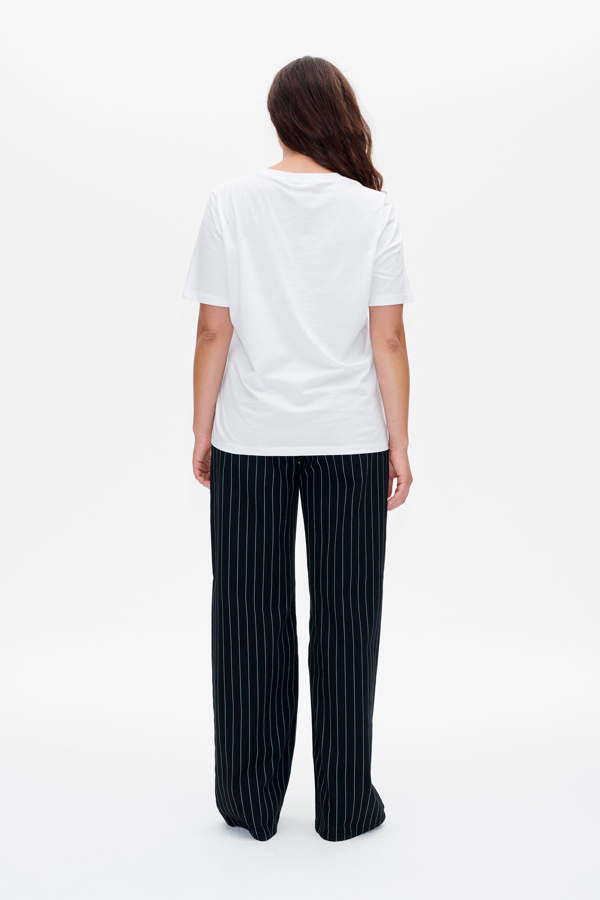 Achteraanzicht van een model in een effen wit T-shirt met korte mouwen en een donkere, wijde broek met fijne verticale strepen.