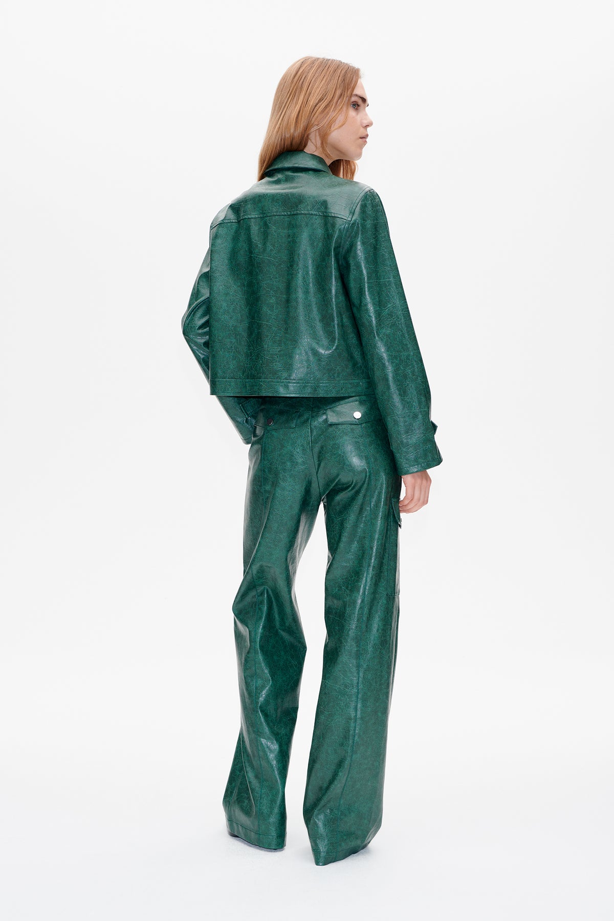 Model in a mottled dark green jacket and matching trousers, shown from behind with the jacket's collar and back seams visible.