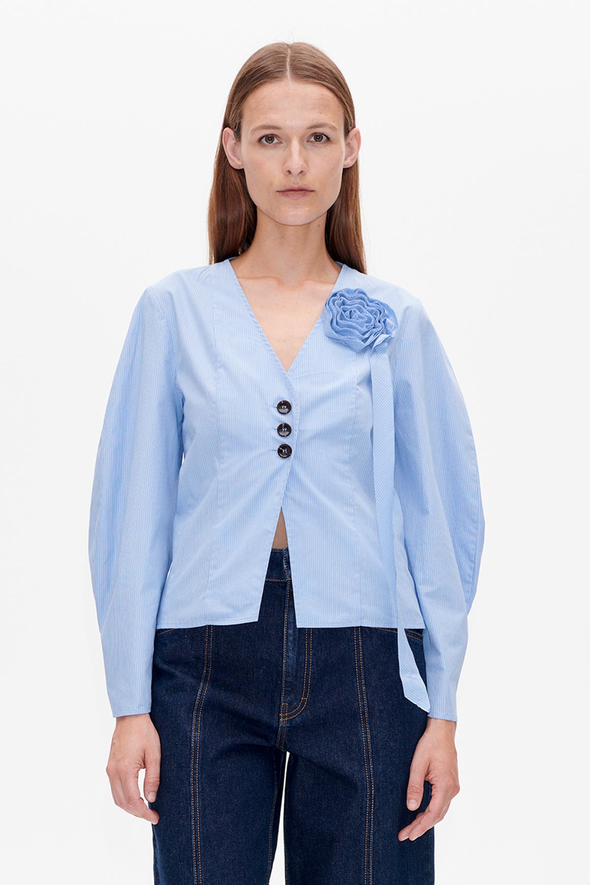 Front view of a light blue pinstriped blouse with a V-neck, dark buttons, a fabric flower and long sleeves.