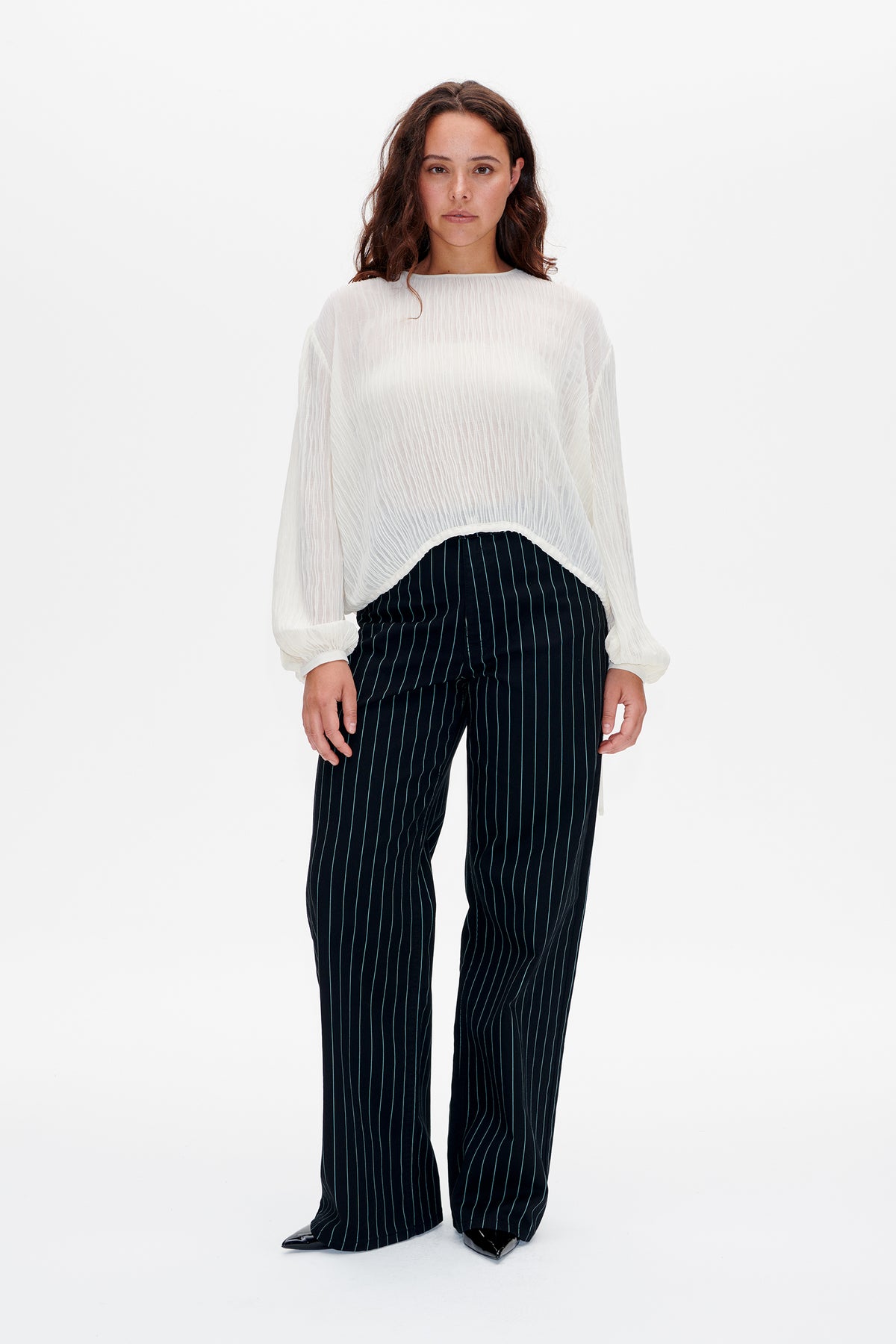 Front view of a model wearing a white textured blouse with long gathered sleeves and navy wide-leg trousers with fine vertical pinstripes.