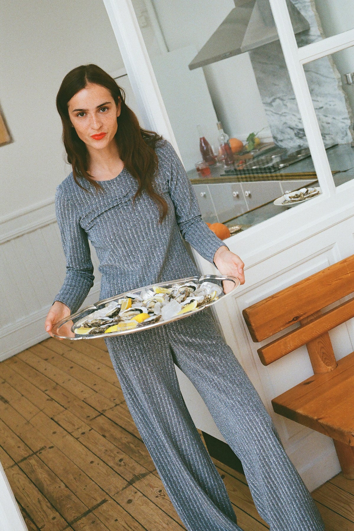 Model holding a platter in a kitchen, wearing a grey ribbed long-sleeve top and matching wide-leg trousers.