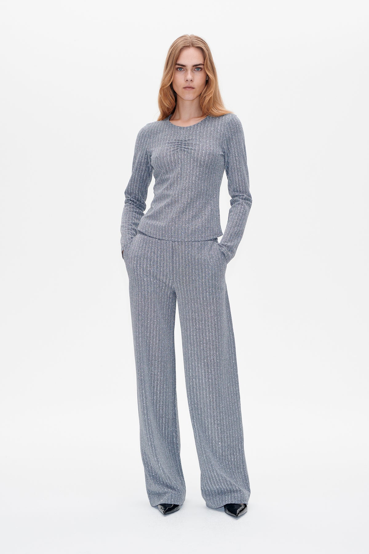 Front view of a model wearing a shimmering silver-gray ribbed long-sleeve top with a gathered chest detail and matching wide-leg trousers.