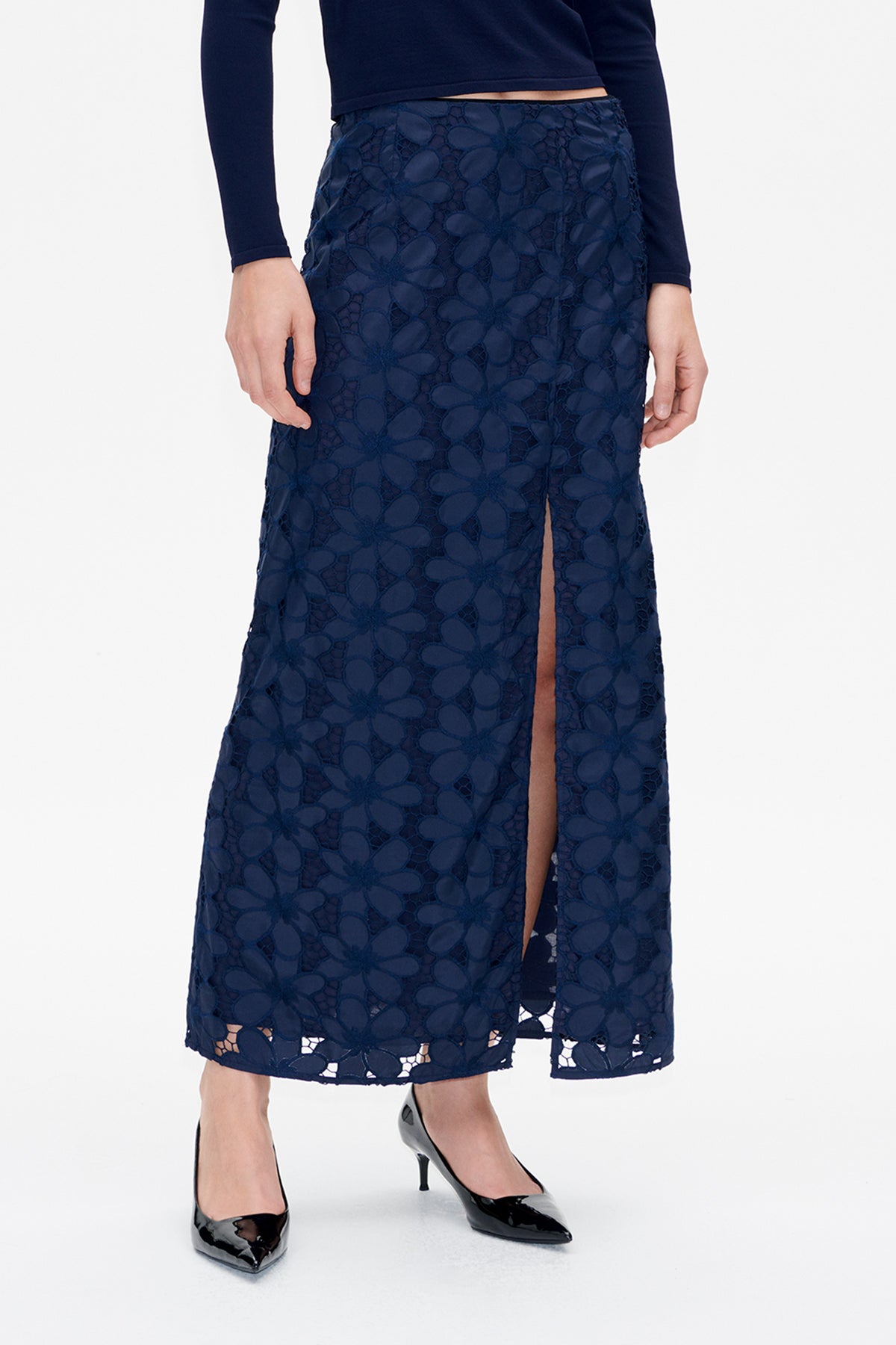 Front detail of a navy midi skirt with raised floral lace-like pattern and a high side slit, worn with a dark long-sleeve top.