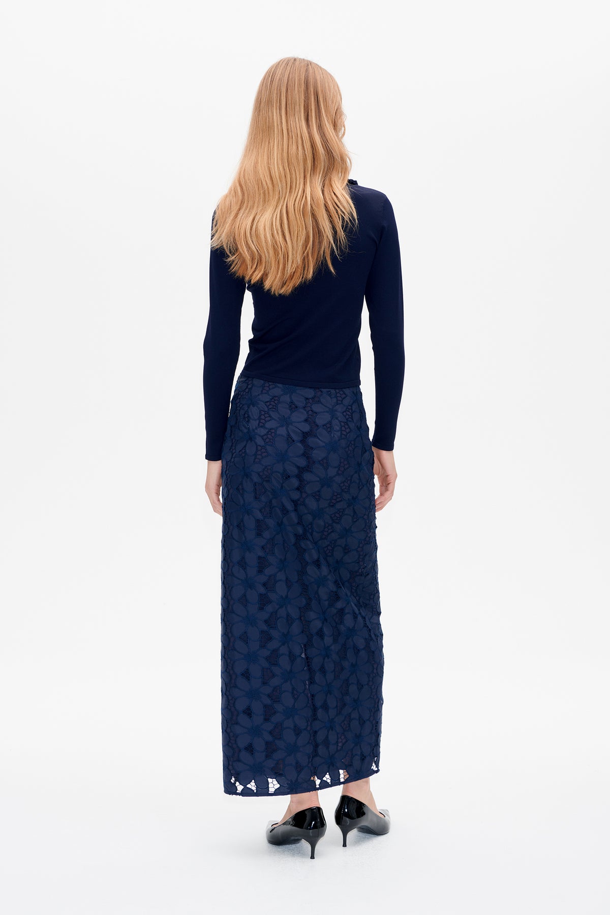 Back view of a model wearing a fitted navy long-sleeve top and a navy floral lace ankle-length skirt.