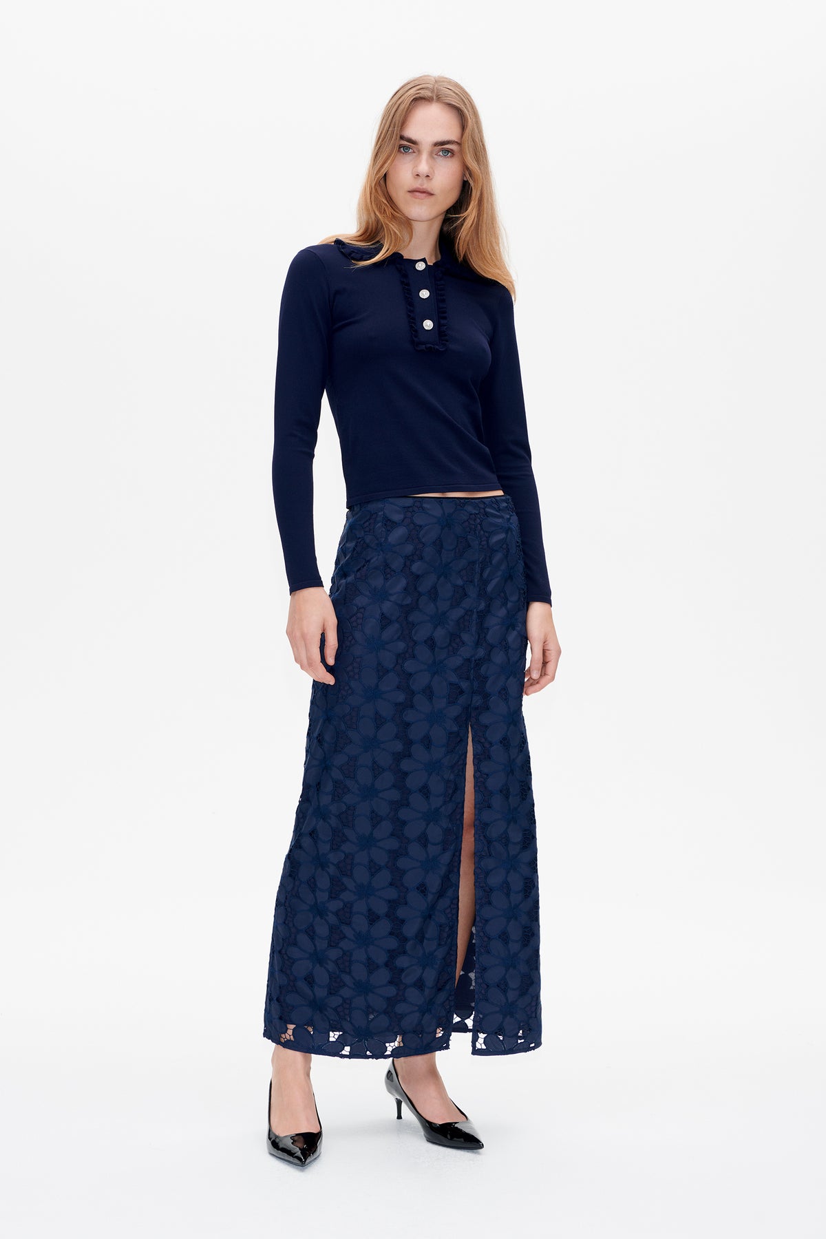 Model wearing a navy long-sleeve top with ruffled placket and decorative buttons, paired with a navy floral lace midi skirt with a front slit.