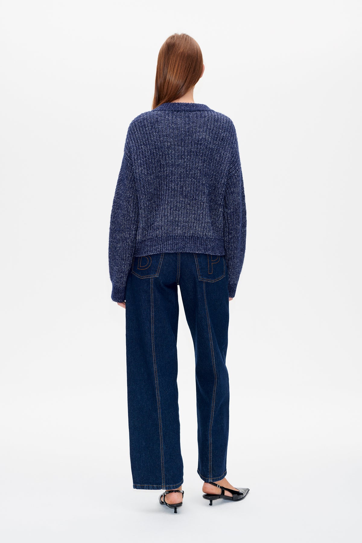Achteraanzicht van een model dat een marineblauwe, structuurgebreide trui draagt met donkere, wijde jeans.