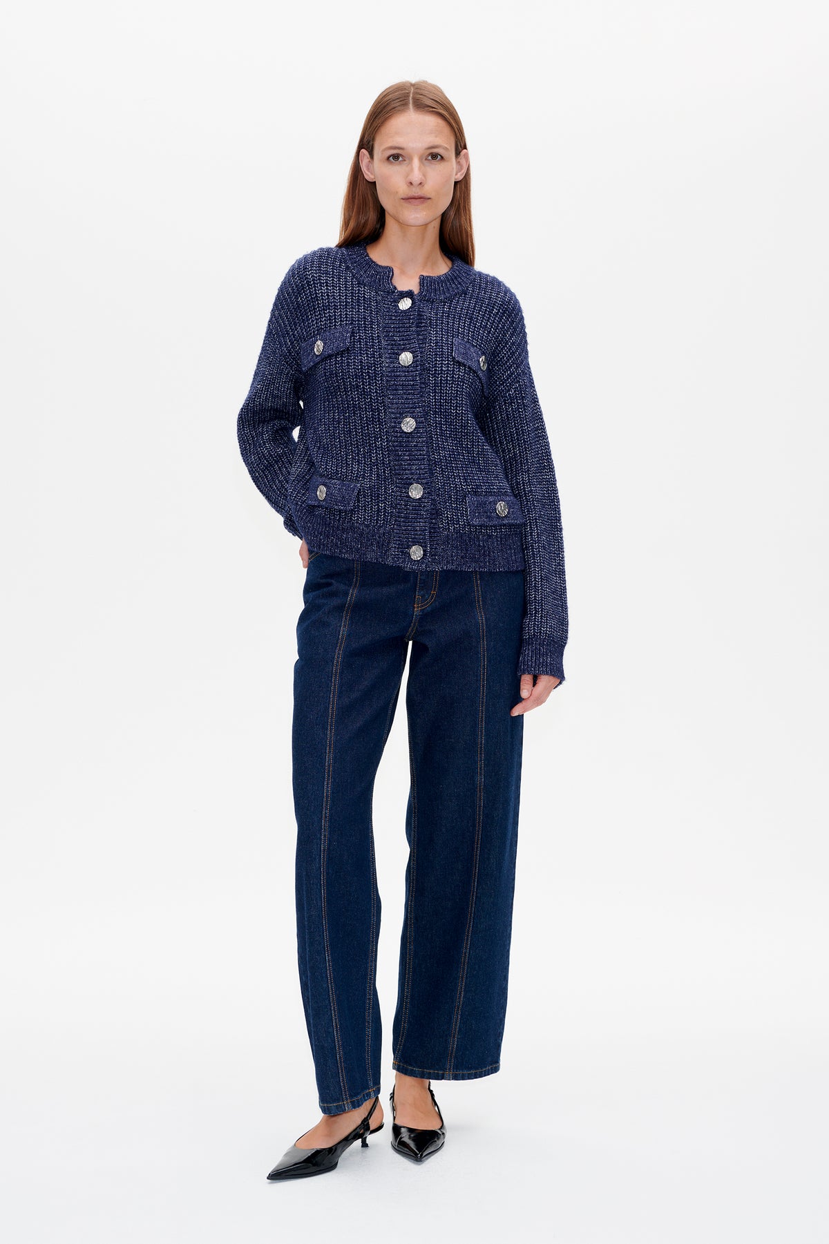 Vooraanzicht van een model dat een marineblauw gebreid vest met structuur, zilveren knopen en klepzakken draagt, gecombineerd met donkere jeans.