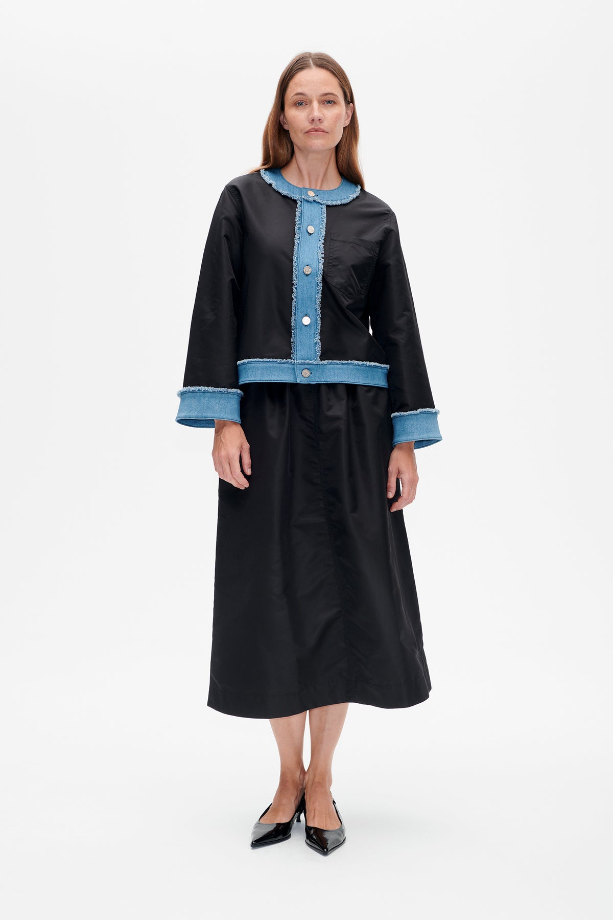 Front view of a black long-sleeved midi dress with blue denim trim, frayed edges, button front and chest pocket.