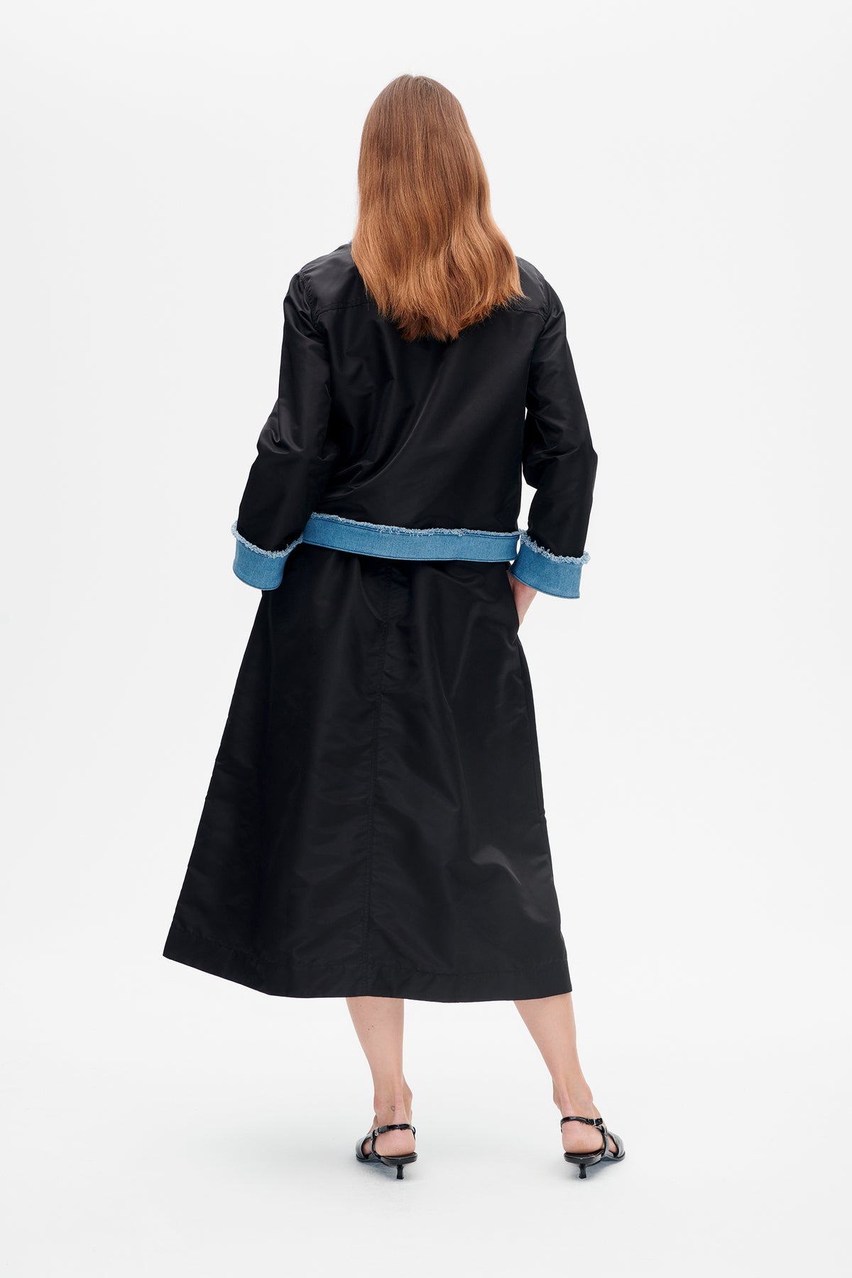 Back view of a black long-sleeved midi dress with blue denim trim and frayed edges at the waist and cuffs.
