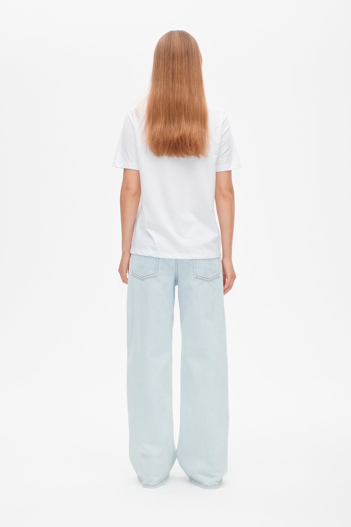 Achteraanzicht van een effen wit T-shirt met korte mouwen, gestyled met lichtblauwe jeans met wijde pijpen.