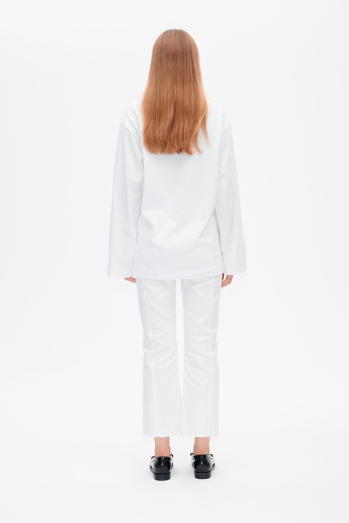 Back view of a model wearing a plain white long-sleeved top and cropped white trousers.