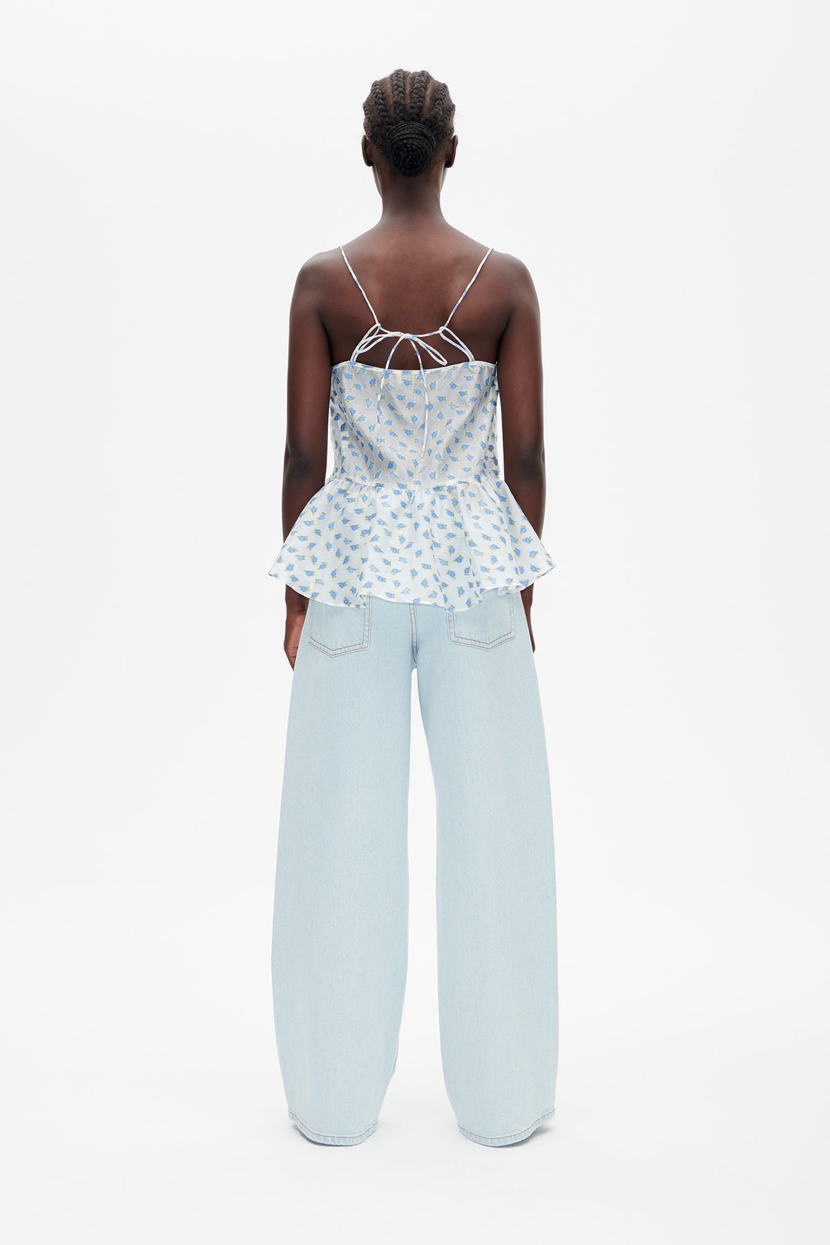 Back view of a white floral-print spaghetti-strap peplum top with a tie back, paired with pale blue wide-leg jeans.