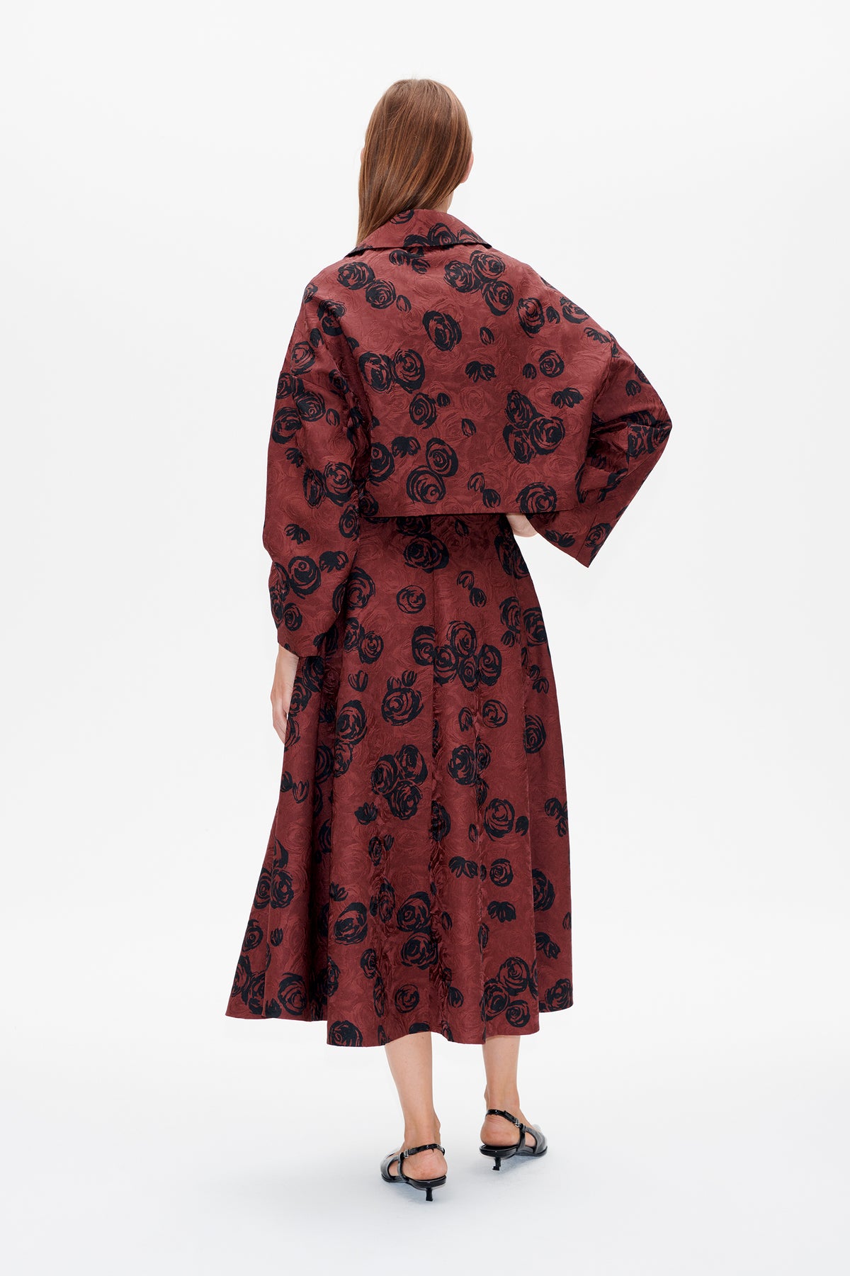 Back view of a model wearing a burgundy midi dress with oversized black rose prints and wide sleeves.