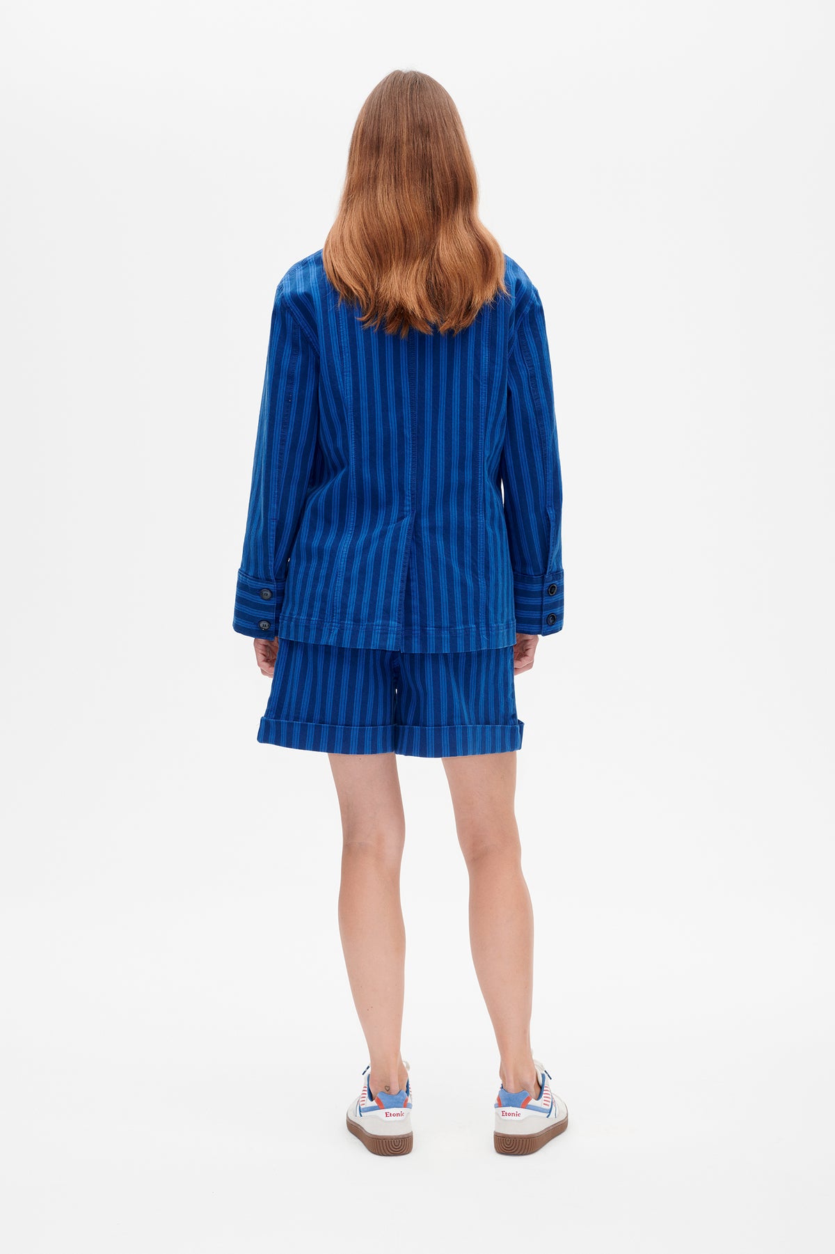 Back view of a model wearing a blue striped long-sleeved jacket and matching cuffed shorts.