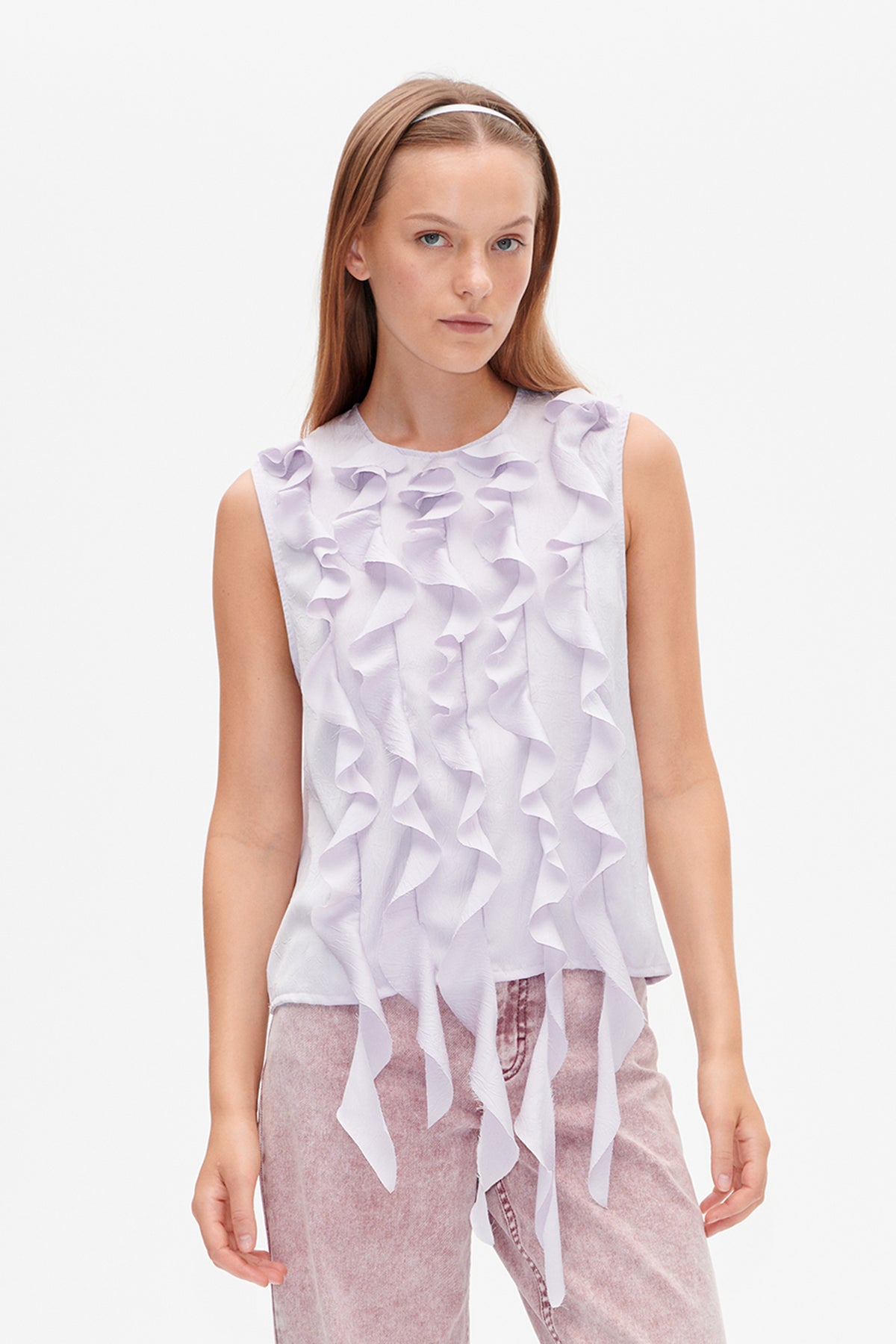 Front view of a sleeveless pale lavender blouse with cascading layered ruffles, styled with mauve trousers.