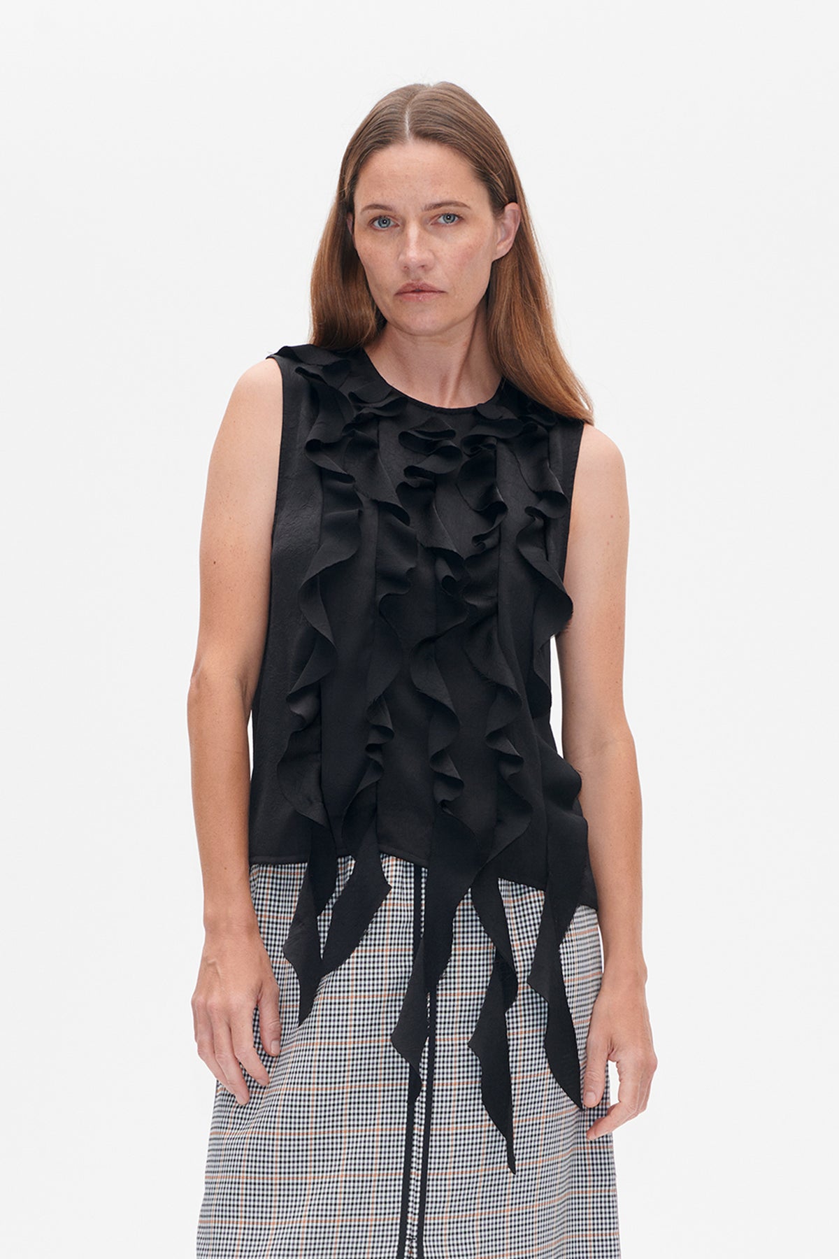 Front view of a sleeveless black top with cascading ruffles and long ties, worn with a fine black-and-white checked skirt crossed by rust stripes.