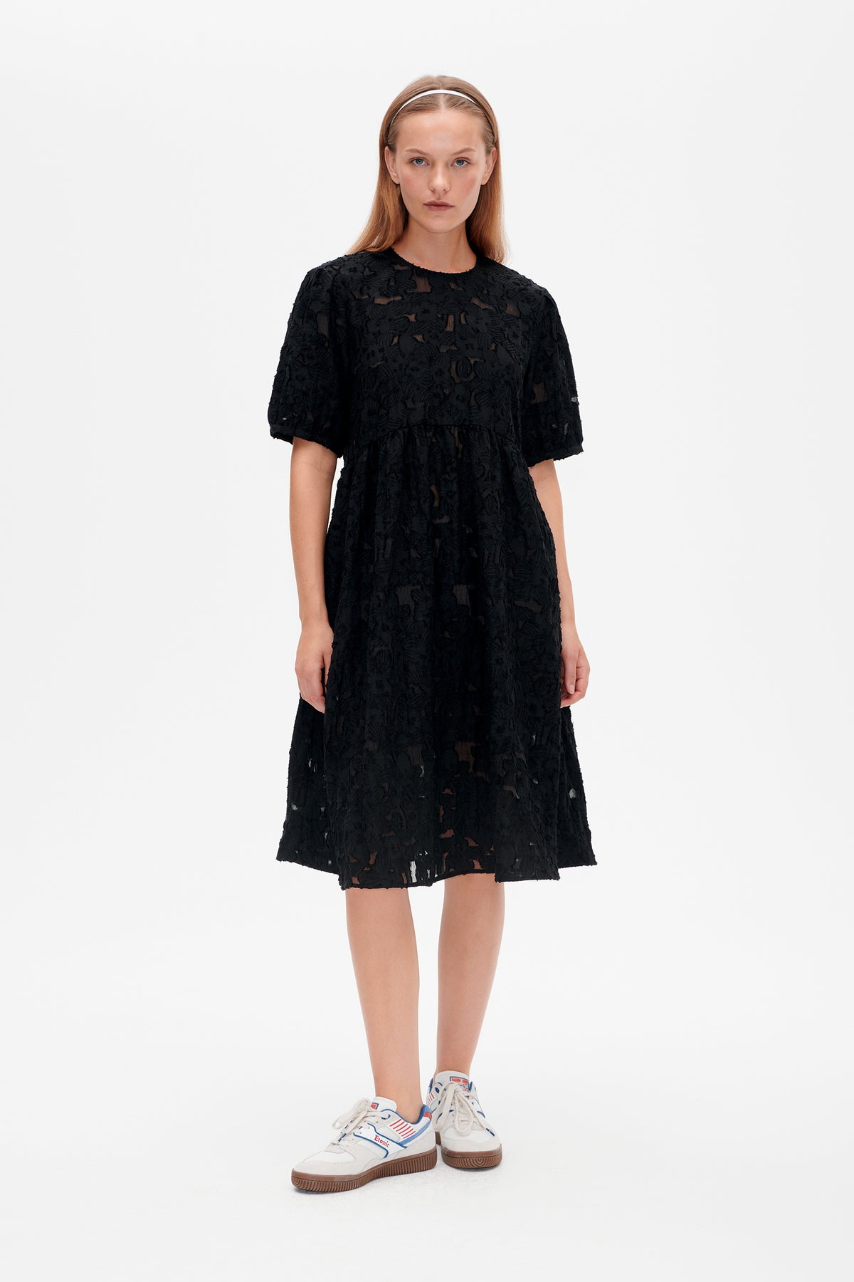 Front view of a black knee-length dress with a raised floral pattern, sheer sections, a round neckline and short sleeves.