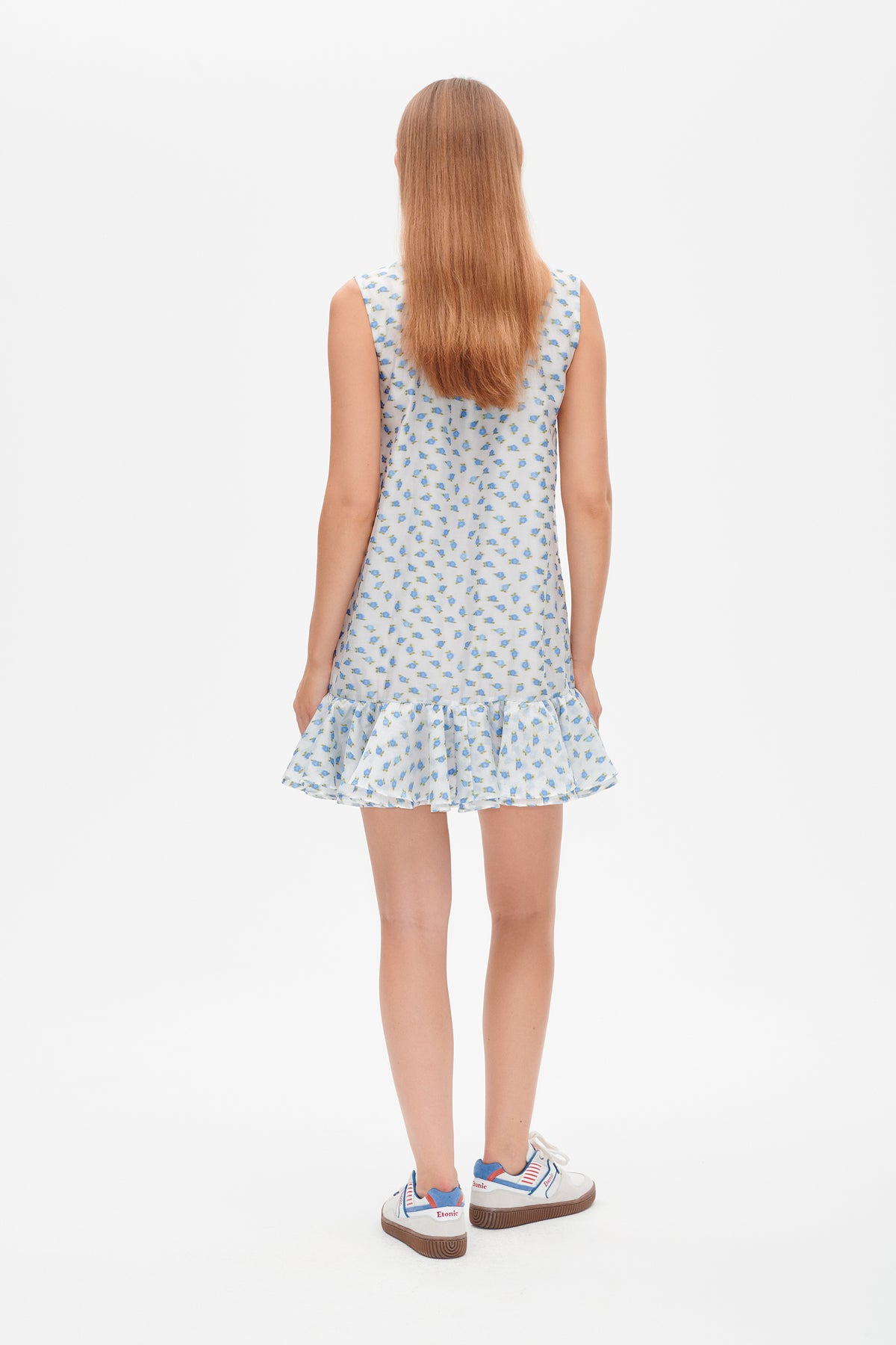 Back view of a sleeveless white mini dress with a small blue and green floral print and a ruffled hem.