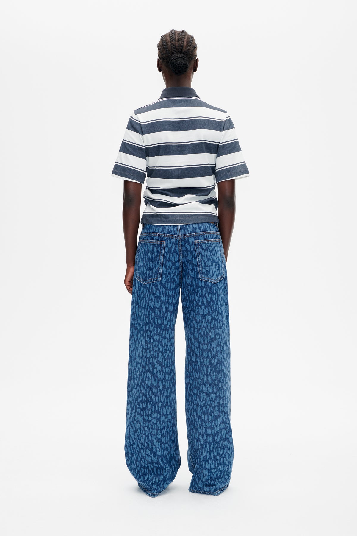 Back view of a model wearing a navy-and-white striped short-sleeve collared shirt and wide-leg blue patterned jeans.