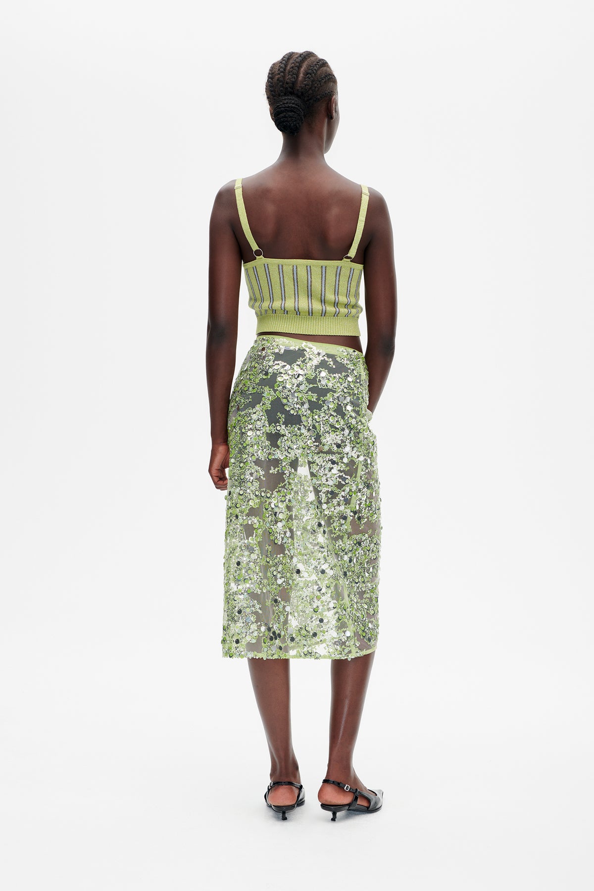 Back view of a model wearing a lime-green striped knit camisole and a sheer green skirt densely embellished with sequins.