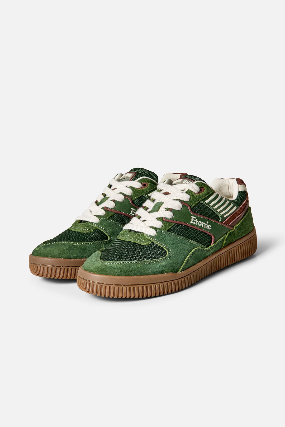 Donkergroene lage sneakers met witte veters, contrasterende panelen, crèmekleurige strepen en bruine rubberen zolen, getoond van voren en opzij.