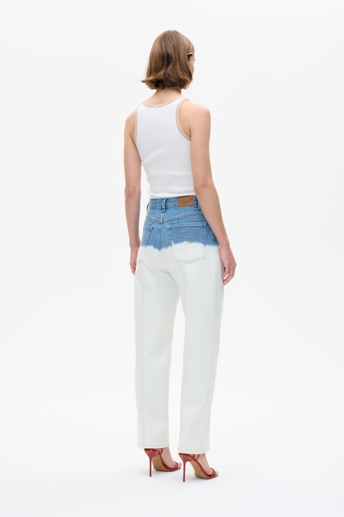 Rückenansicht eines Models, das ein weißes Tanktop mit beiger Einfassung und eine weit geschnittene, zweifarbige Jeans in Blau und Creme trägt.