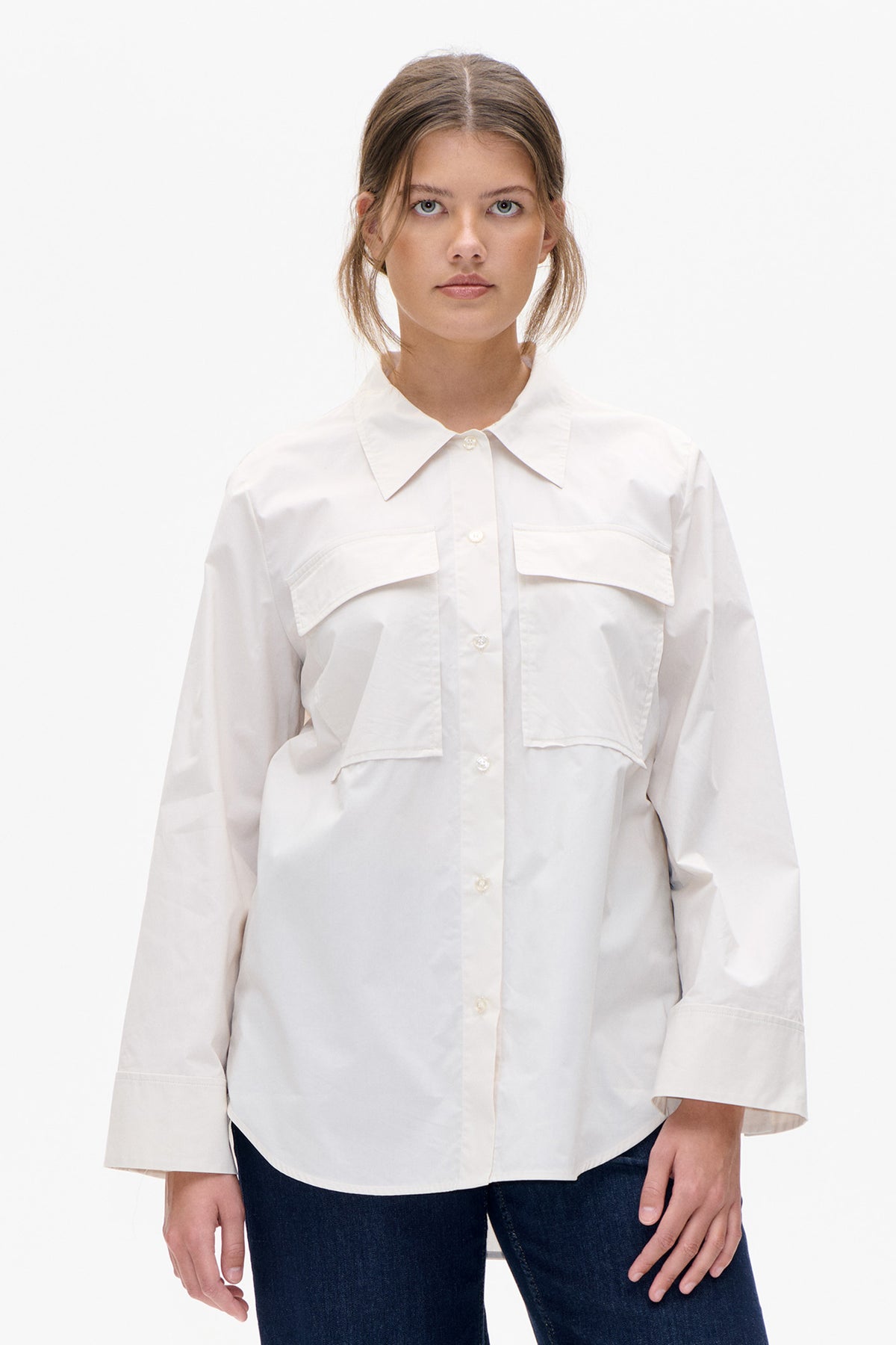 Front view of a white button-front shirt with an oversized pointed collar, short sleeves and two angular flap chest pockets, worn with dark jeans.