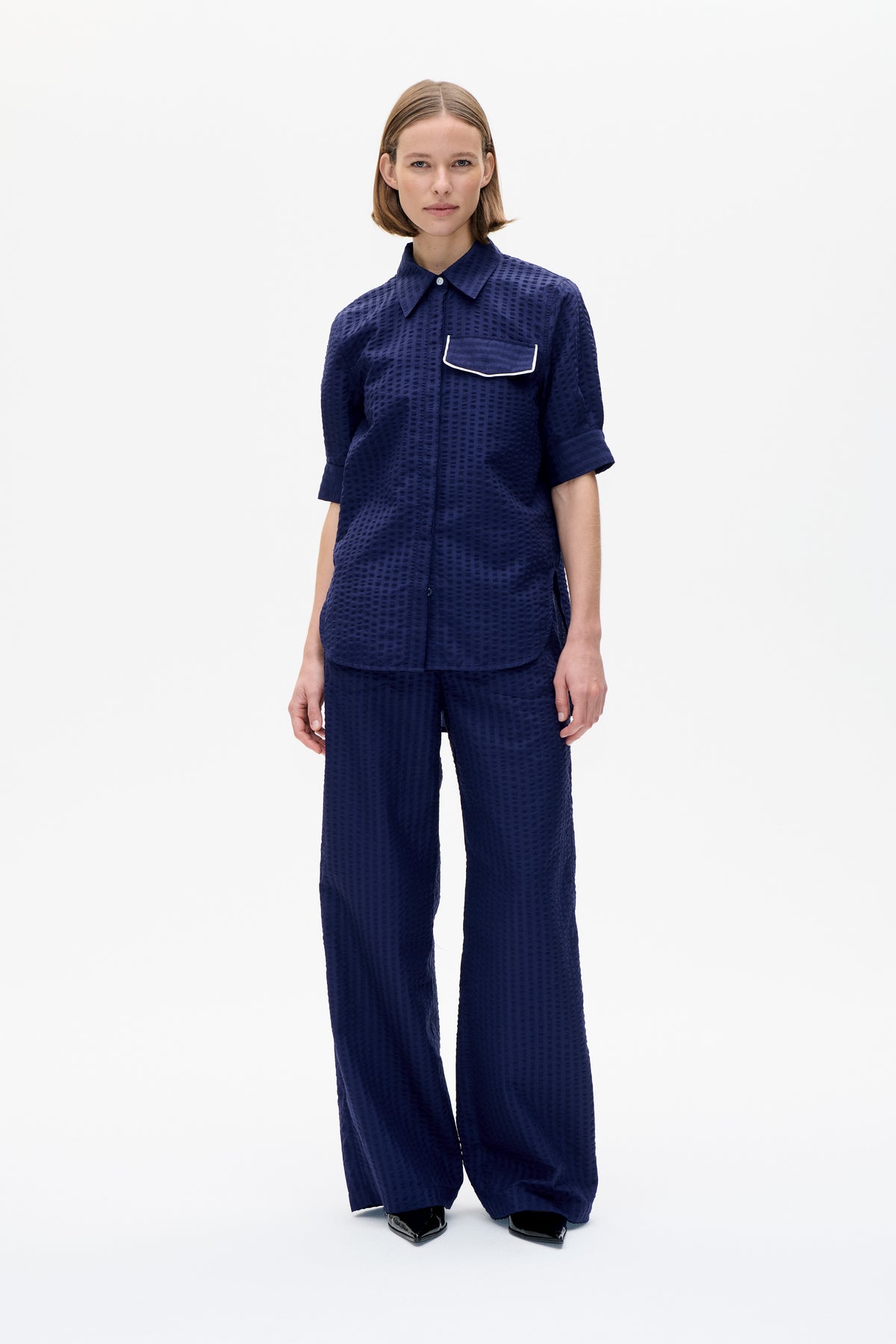 Front view of a model wearing a navy textured short-sleeve shirt with a white-trimmed pocket and matching wide-leg trousers.