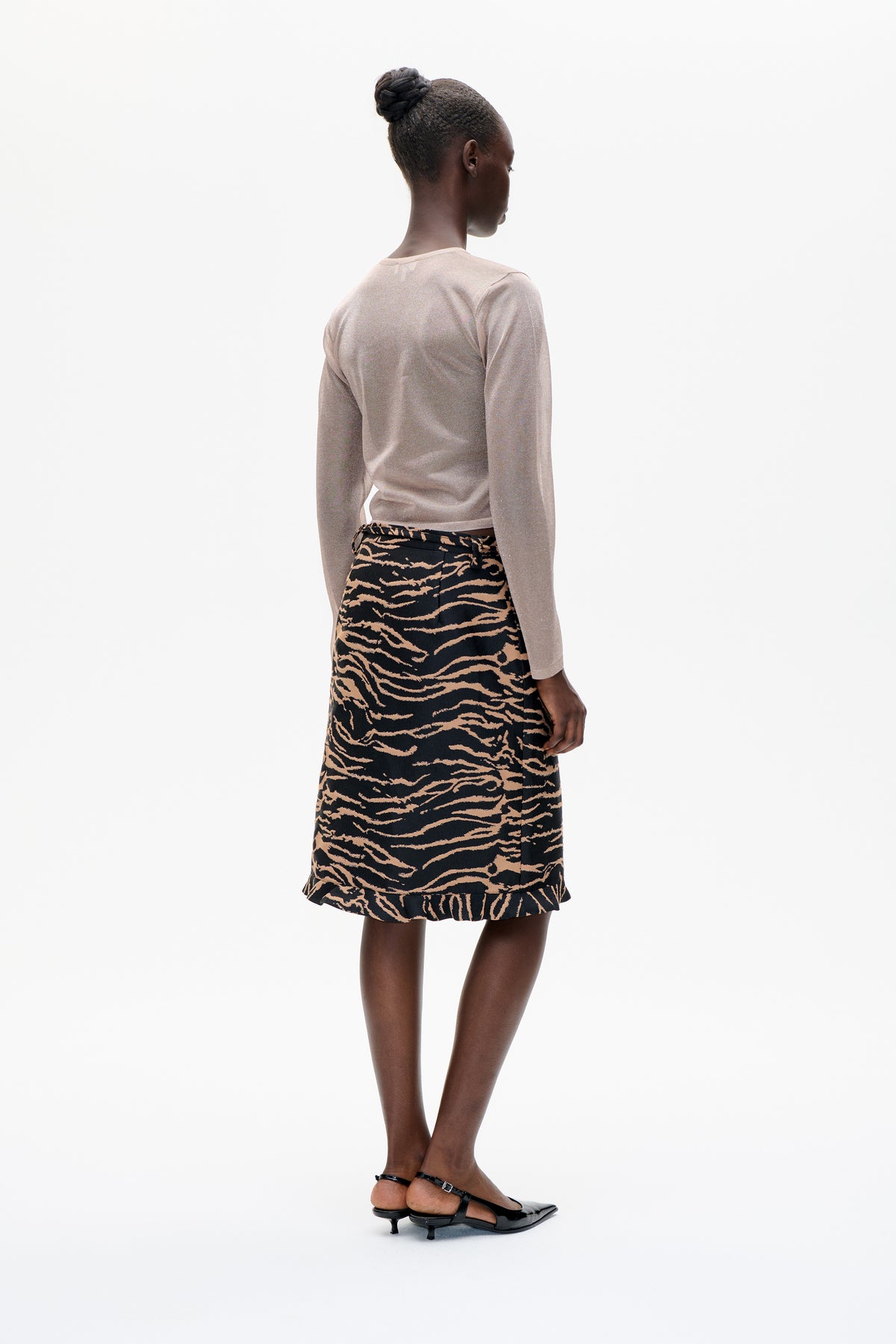 A model seen from behind in a pale blush long-sleeve top and black midi skirt with tan wavy print and a ruffled hem.