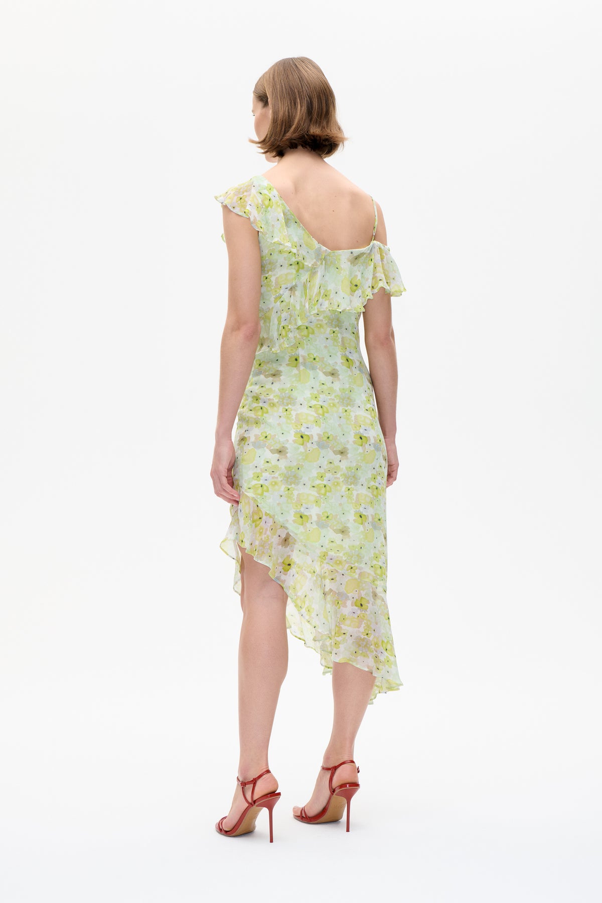 Back view of a pale green and yellow floral dress with a ruffled one-shoulder detail, thin strap and asymmetric hem.