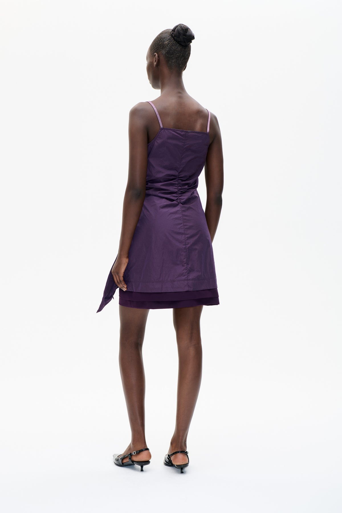 Back view of a model wearing a purple spaghetti-strap dress with pink straps and gathered ruching at the waist.