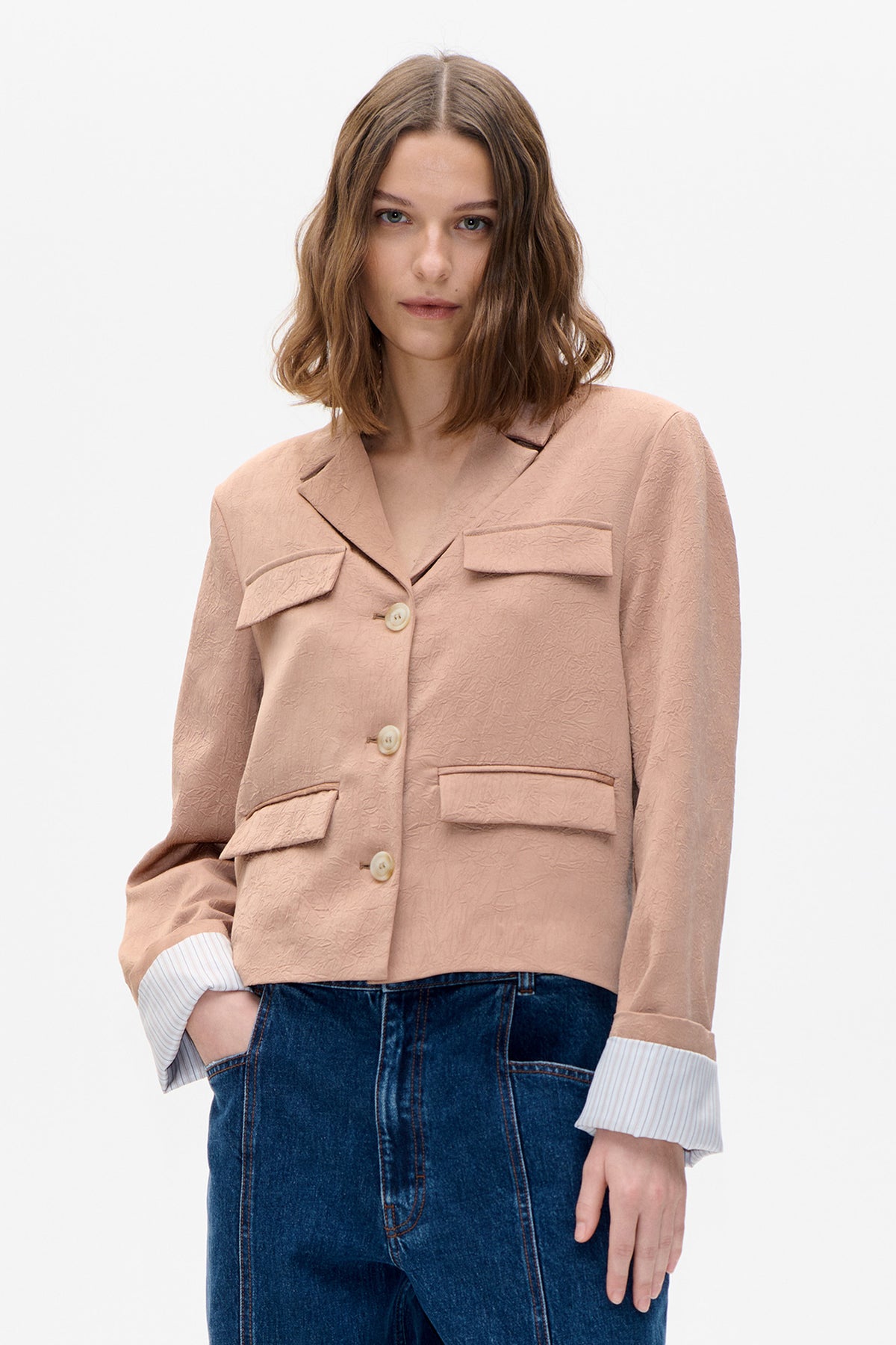 Front detail of a dusty pink textured blazer with notched lapels, flap pockets and light buttons, worn with dark blue jeans.
