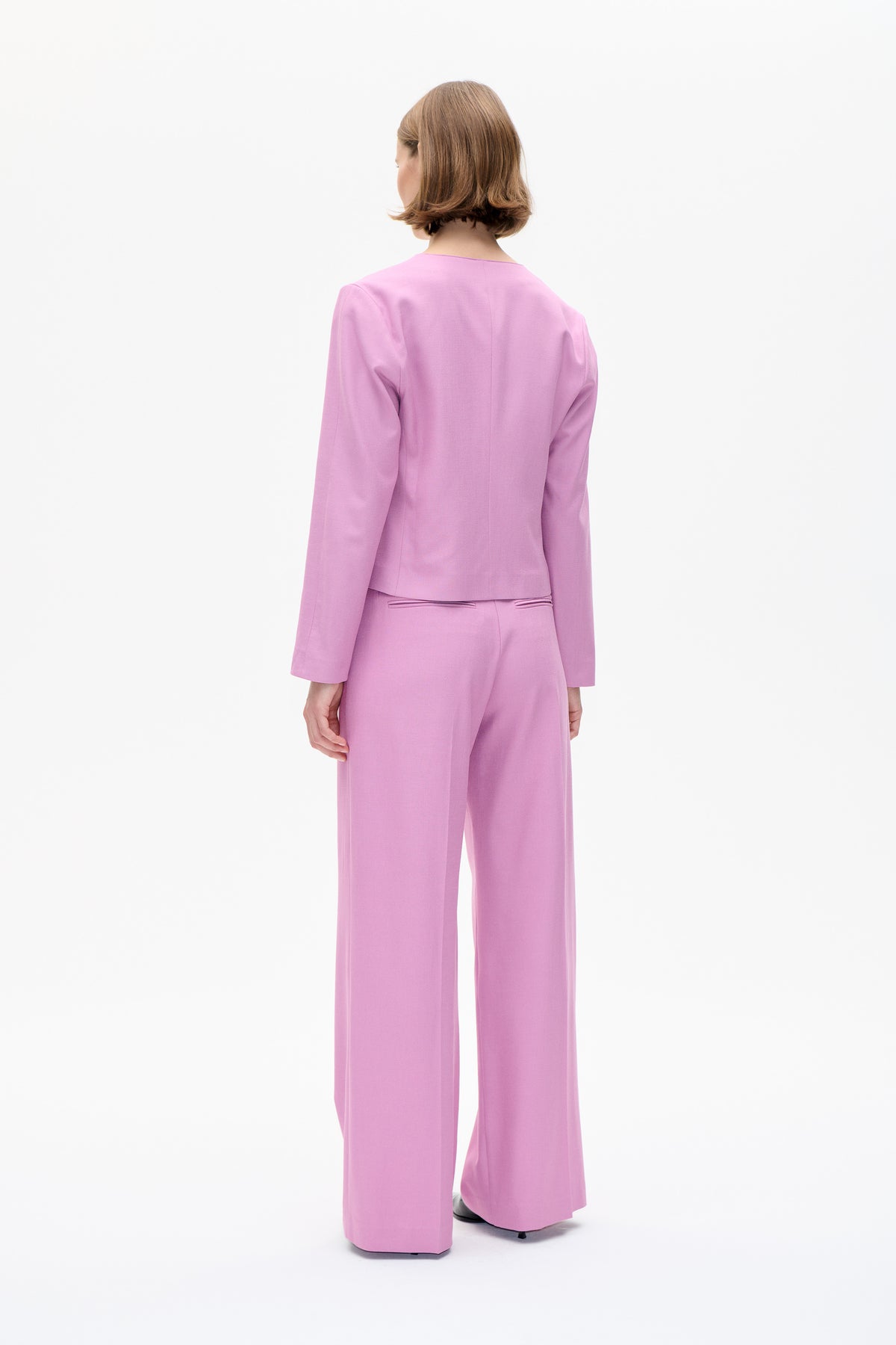 Achteraanzicht van een model met een effen roze getailleerde blazer en een bijpassende broek met wijde pijpen.