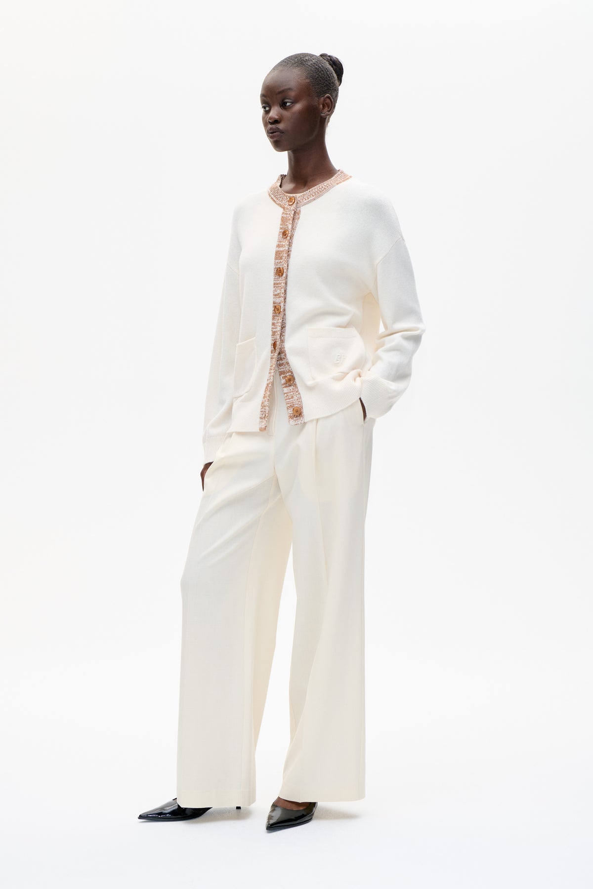 Model wearing an ivory button-front cardigan with tan patterned trim and matching wide-leg trousers, shown full length against a white backdrop.