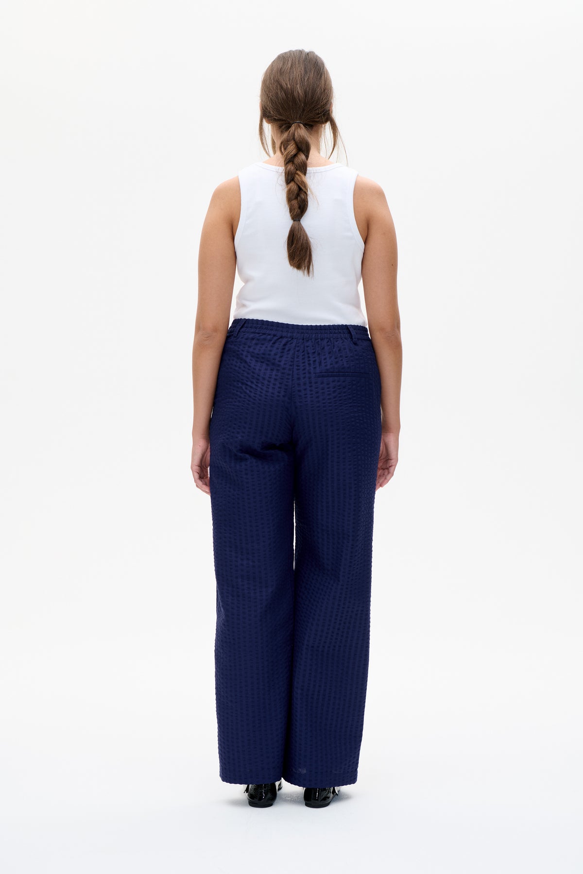 Back view of a white sleeveless top paired with navy wide-leg trousers featuring an elasticated waistband and subtle textured pattern.