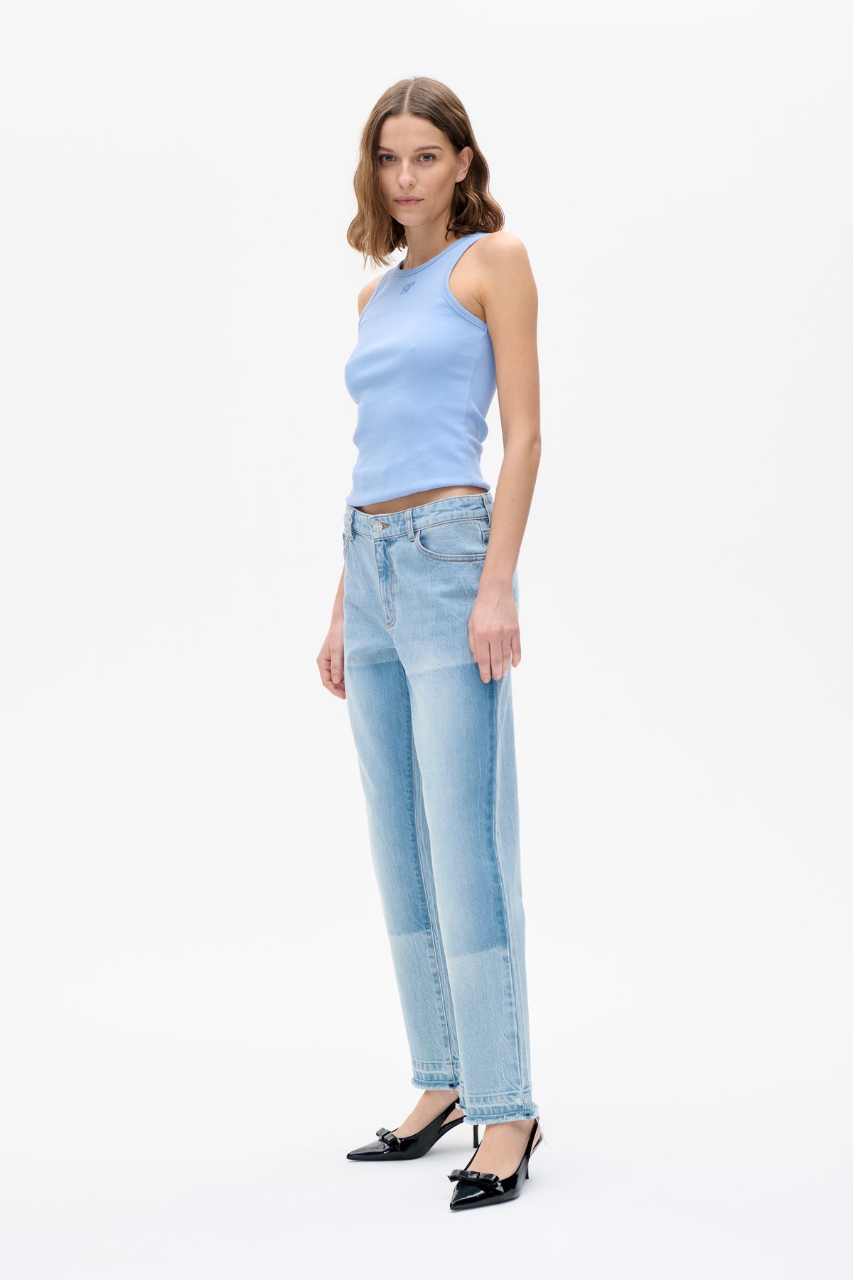 Model wearing a light blue sleeveless top with a small chest logo, light-wash cropped jeans and black bow-detail heels