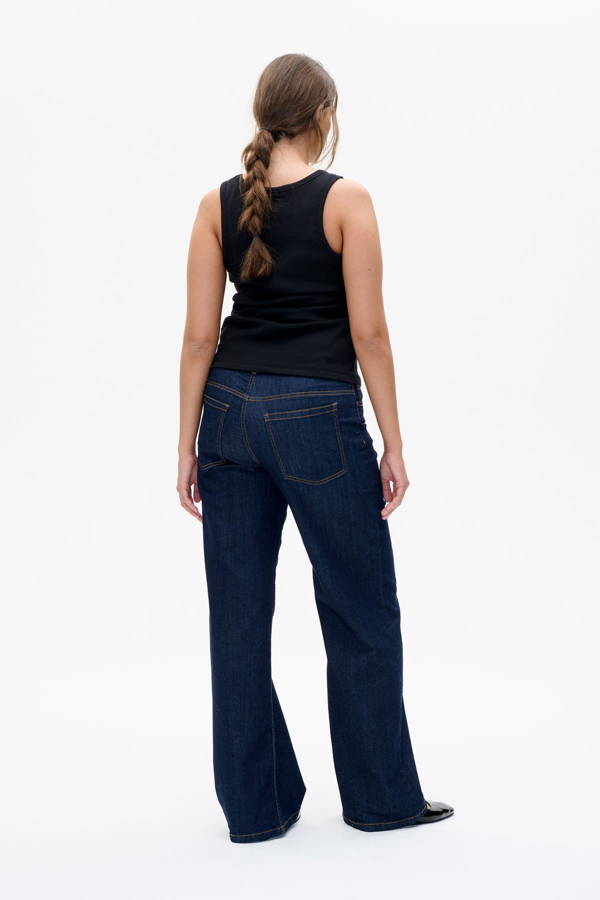 Back view of a model wearing a black sleeveless top and dark indigo wide-leg jeans with contrasting tan stitching.