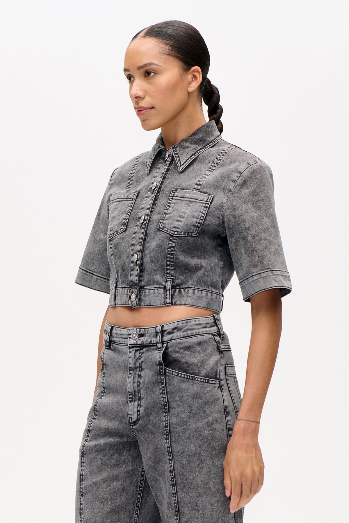 Model wearing a cropped grey acid-wash denim jacket with short sleeves, pointed collar and two chest pockets, shown from the front.