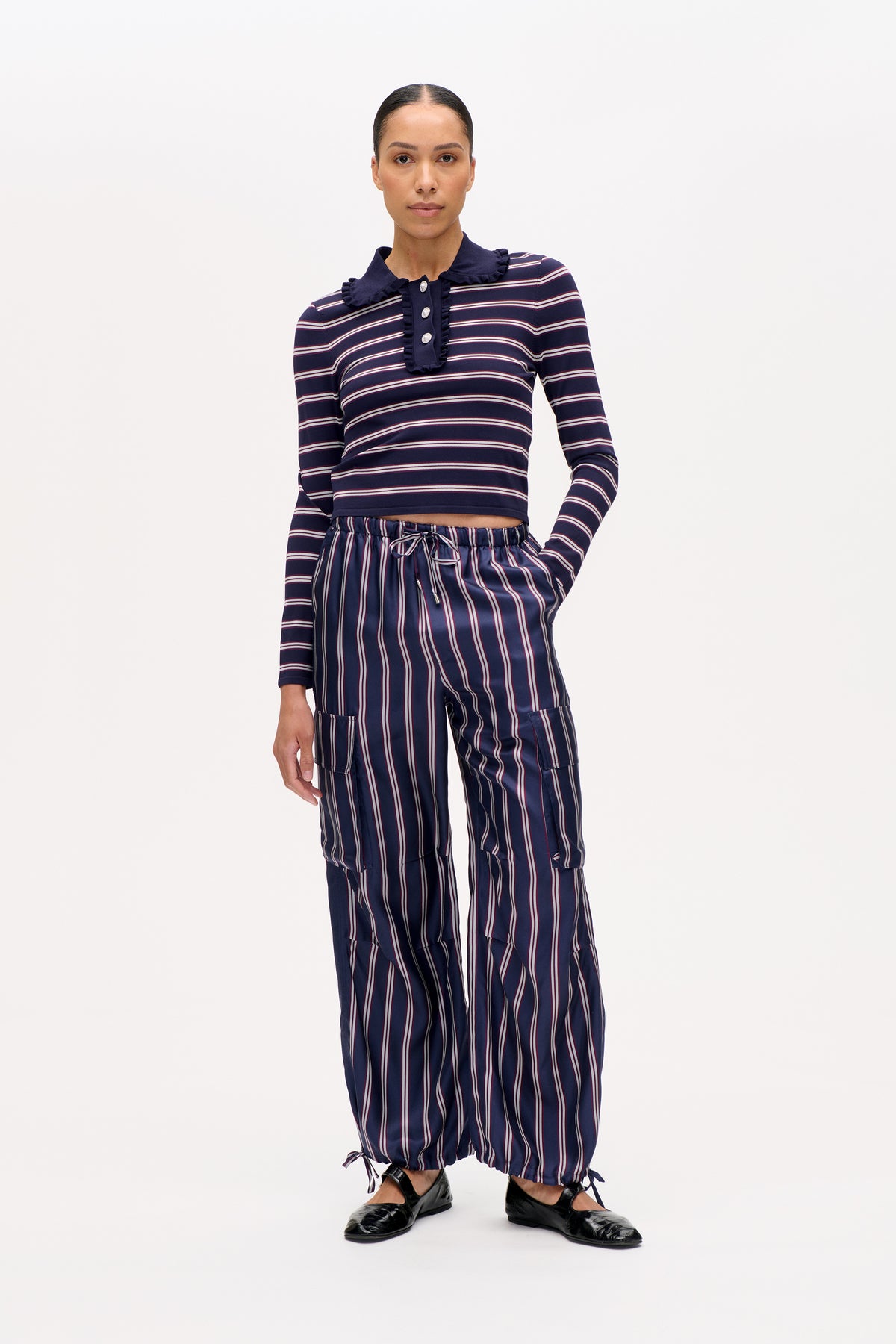 Model wearing a navy long-sleeved top with cream and burgundy stripes, a ruffled collar and placket, and matching vertical-stripe drawstring trousers.