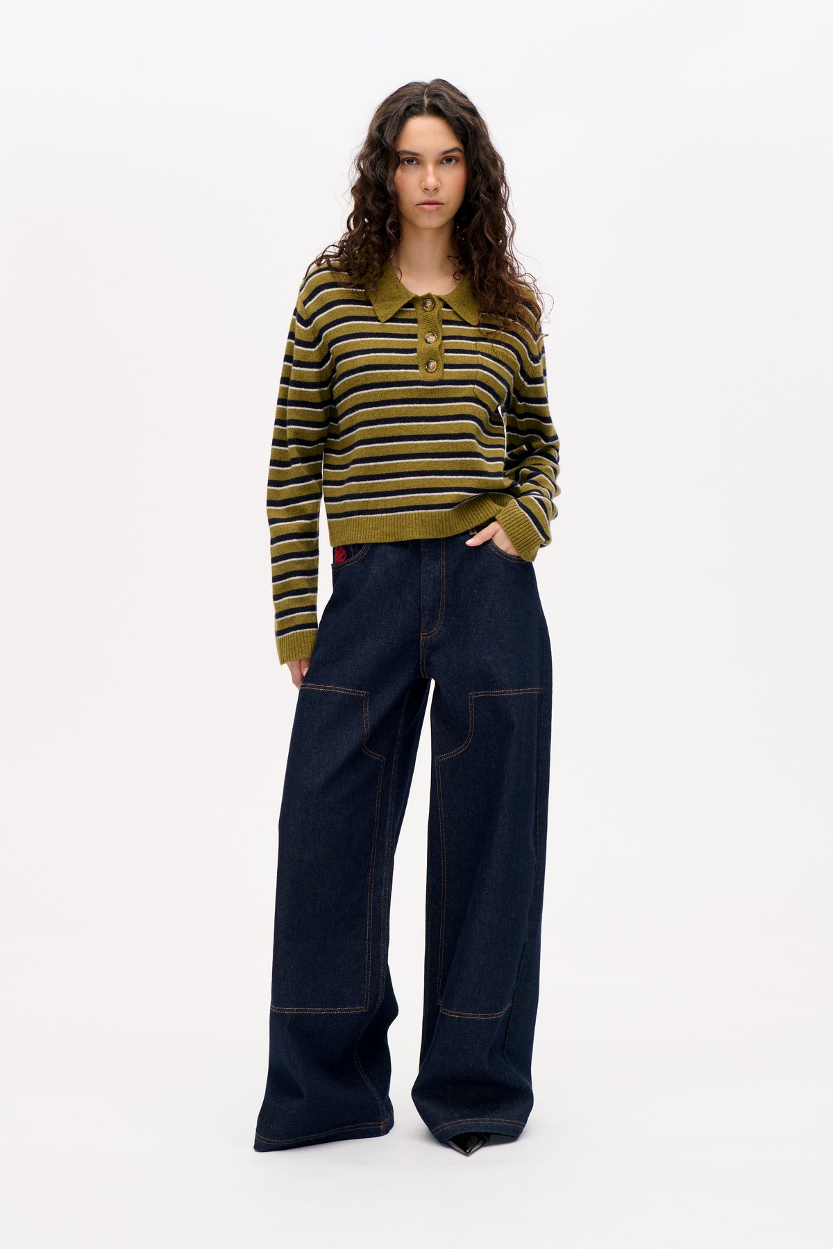 Model wearing an olive green striped long-sleeve knit pullover with a pointed collar and button placket, paired with dark wide-leg jeans.