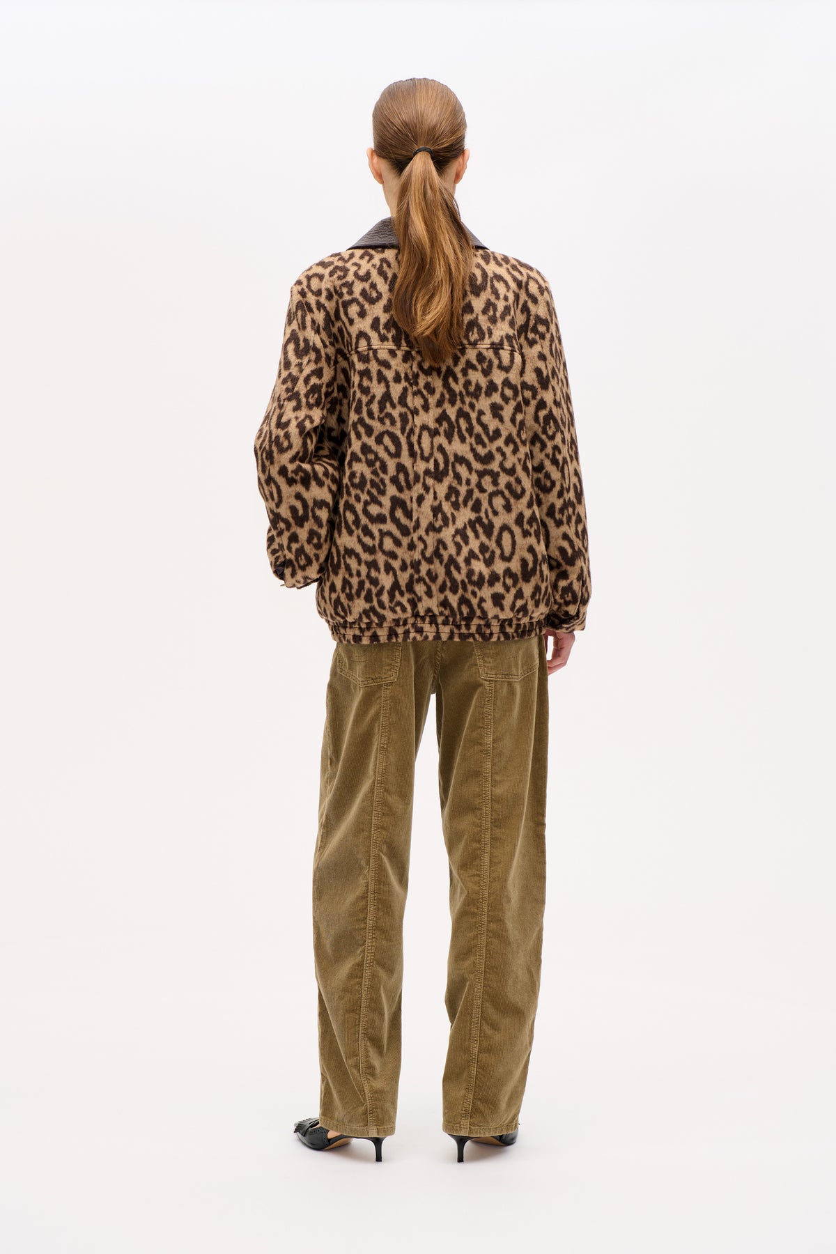 Achteraanzicht van een model in een zandkleurig-donkerbruin luipaardprintjasje met een donkere kraag en een olijfgroene ribfluwelen broek.