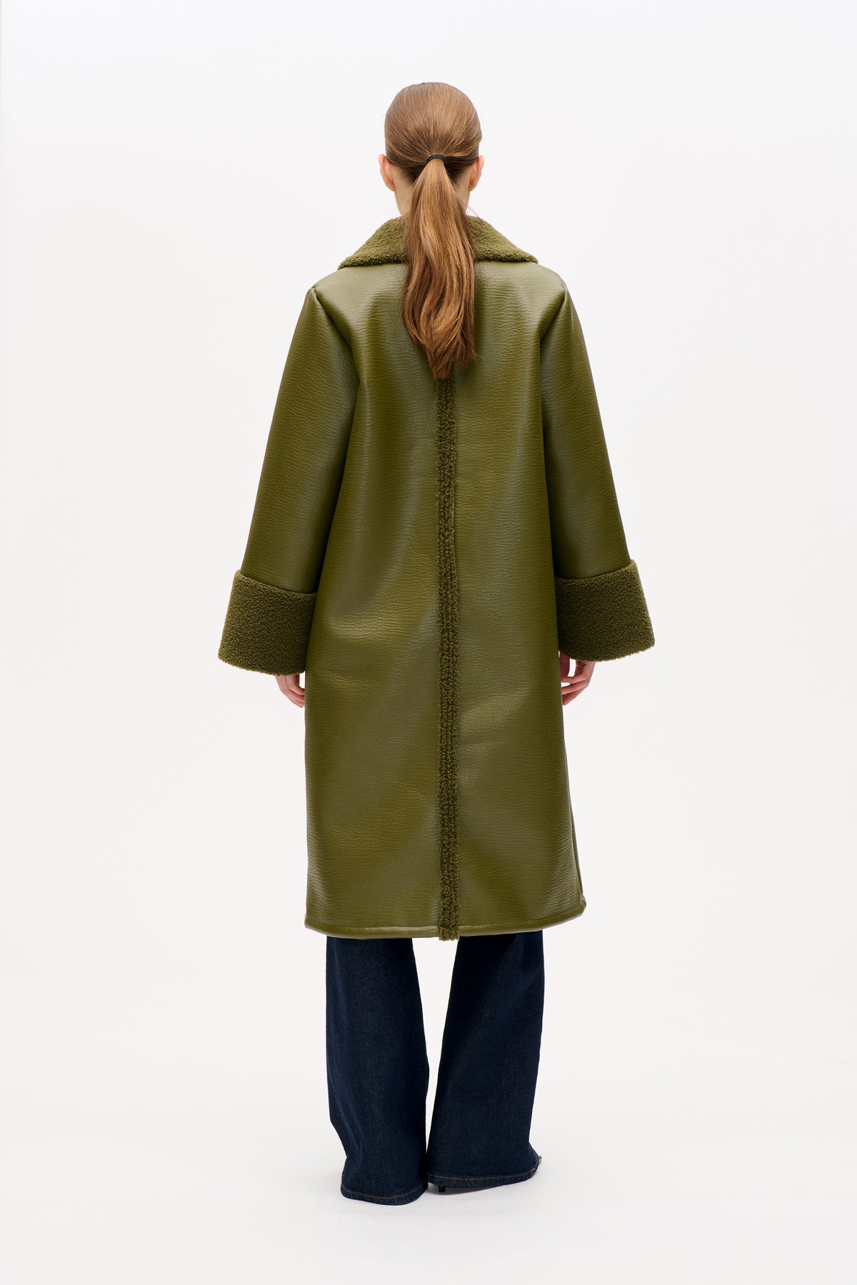 Back view of a long olive-green coat with a textured faux-shearling collar, cuffs and centre seam, worn with dark wide-leg jeans.